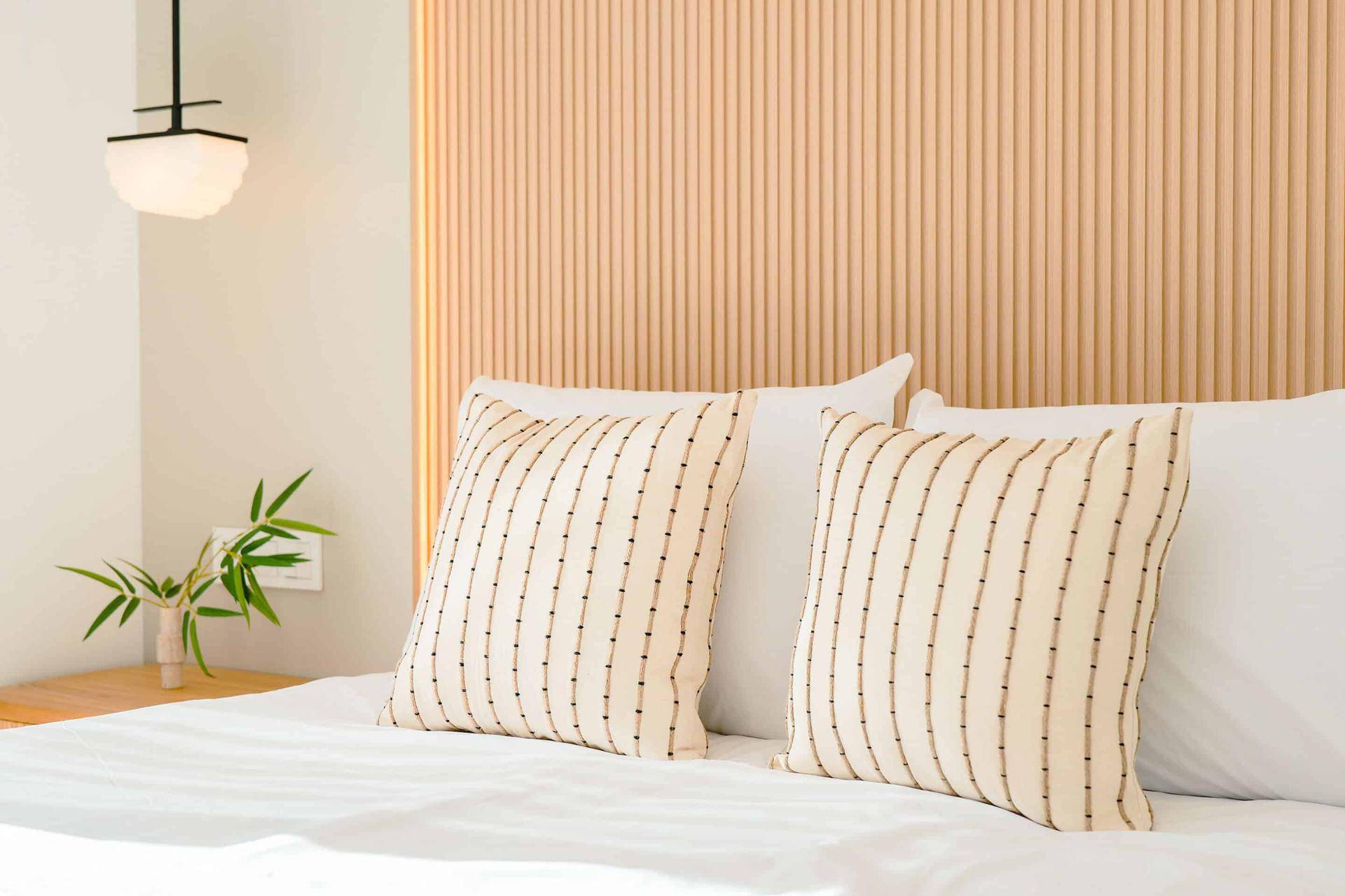 Modernes Schlafzimmer mit hellem Holzpaneel als Kopfteil und minimalistischer Beleuchtung.