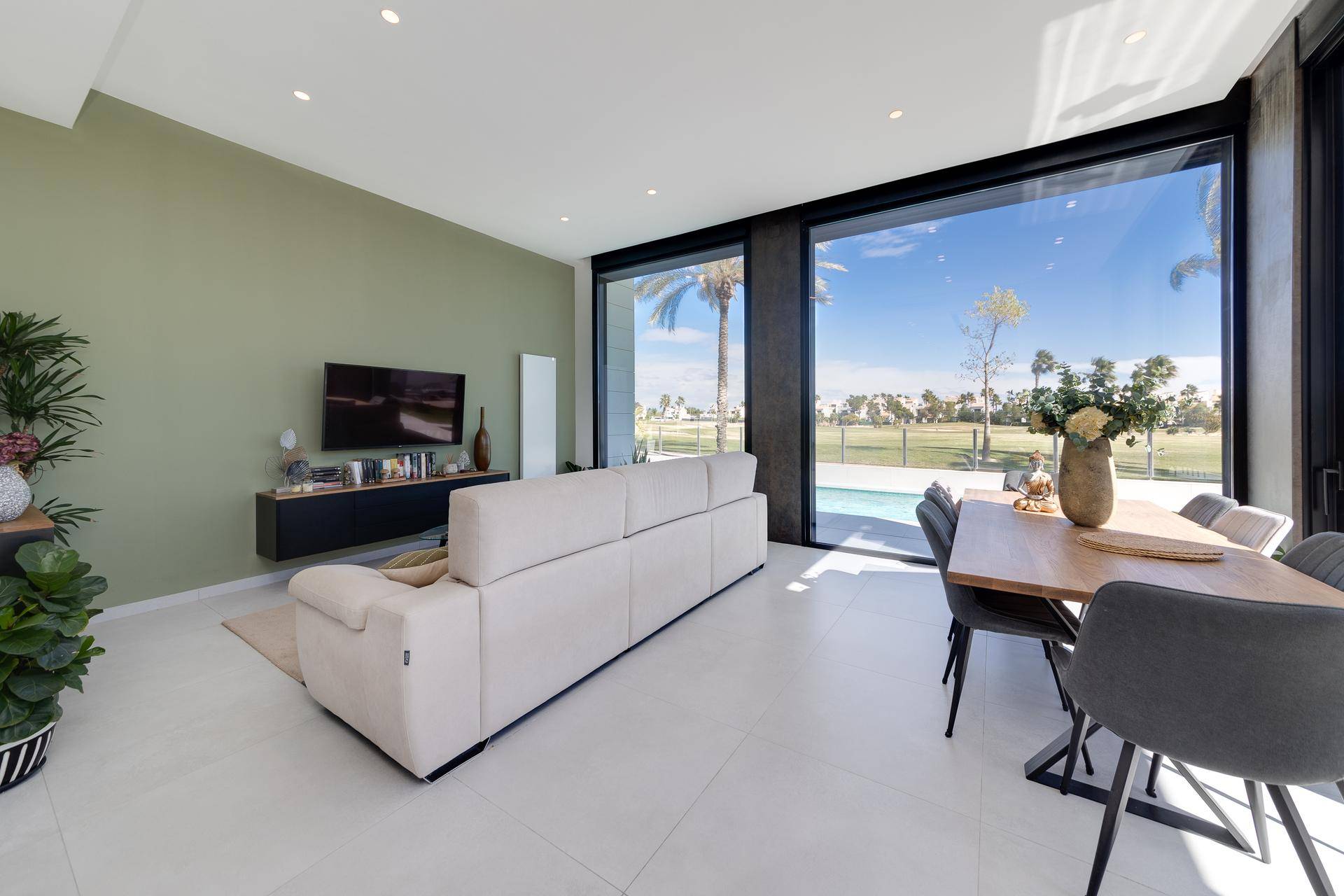 Heller Wohn- und Essbereich mit beigem Sofa und großen Fenstern mit Poolblick.