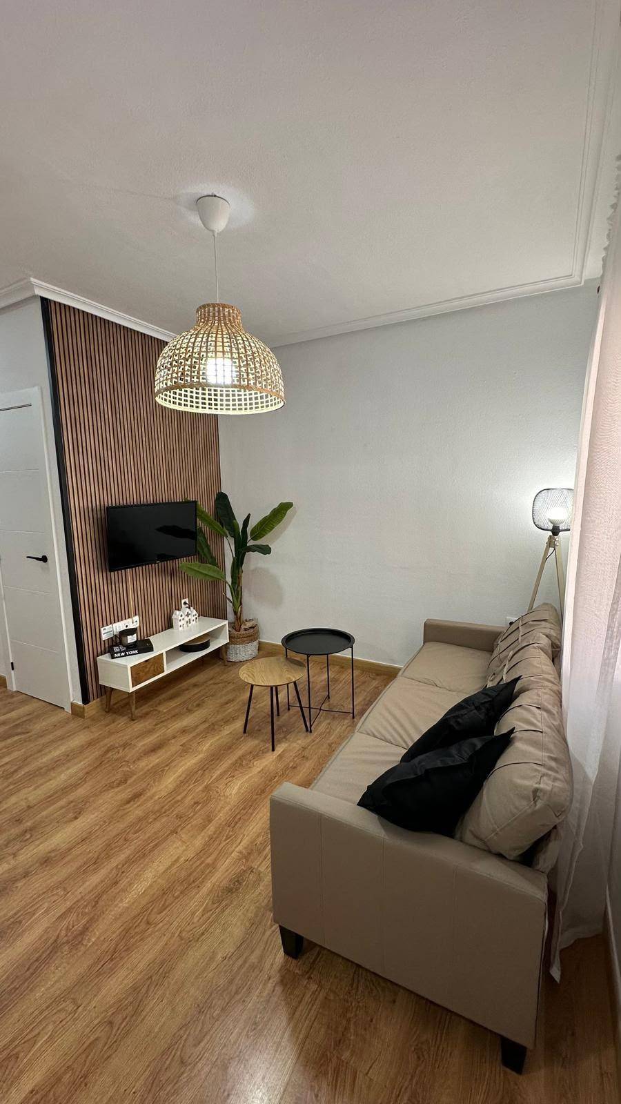 Gemütliches Wohnzimmer mit TV-Wand, beigem Sofa und dekorativer Hängeleuchte.
