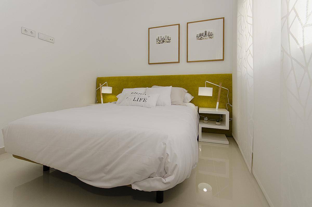Minimalistisches Schlafzimmer mit gelbem Kopfteil, Nachttischen und heller Atmosphäre.
