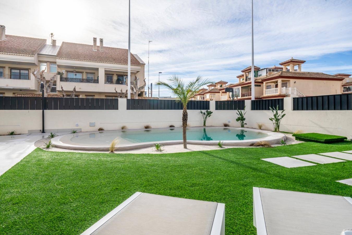Weitläufiger Garten mit Pool, Rasenfläche und Liegestühlen, umgeben von benachbarten Häusern.