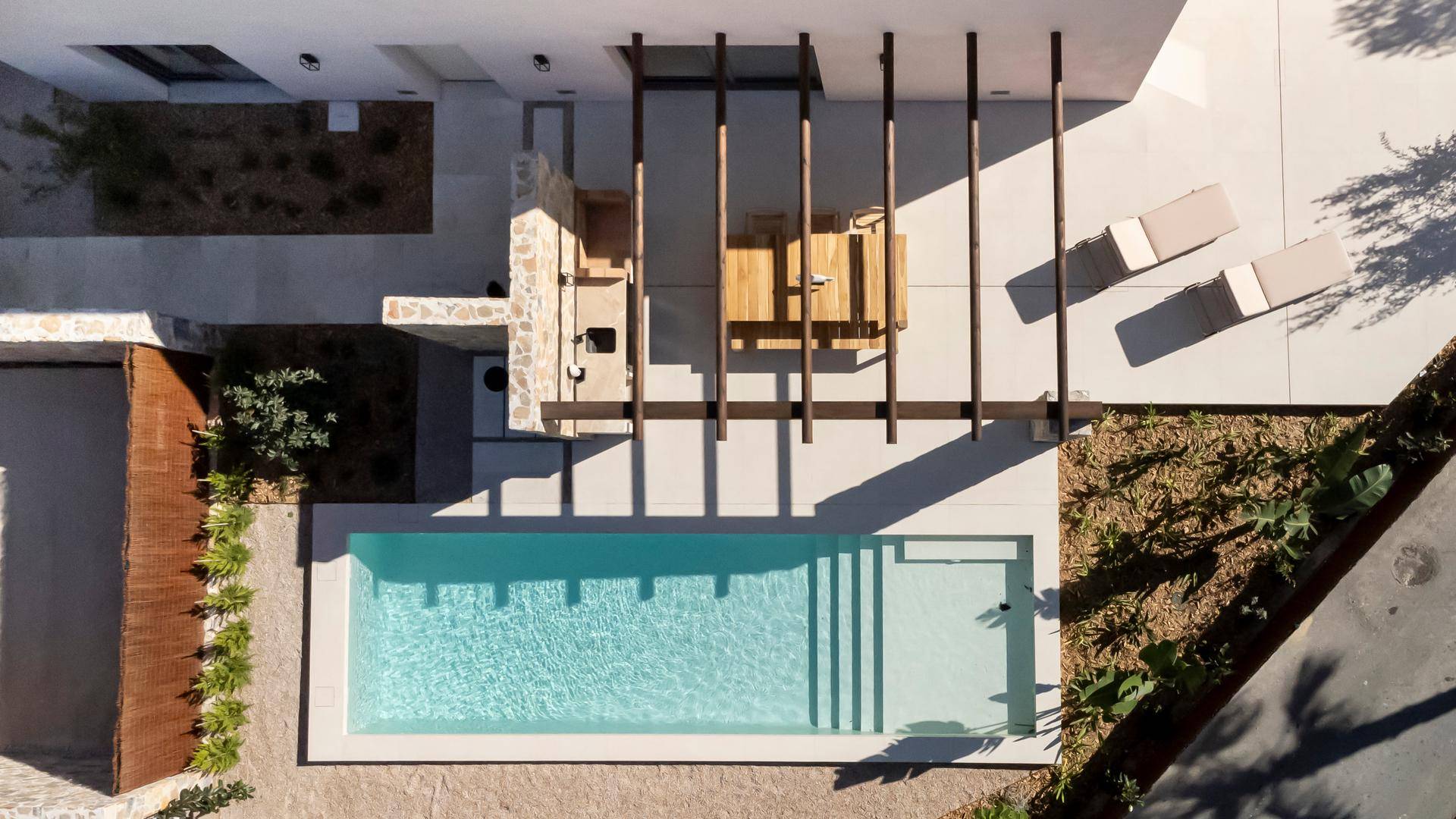Vogelperspektive des Pools und der Sonnenterrasse mit Liegestühlen und Pergola.