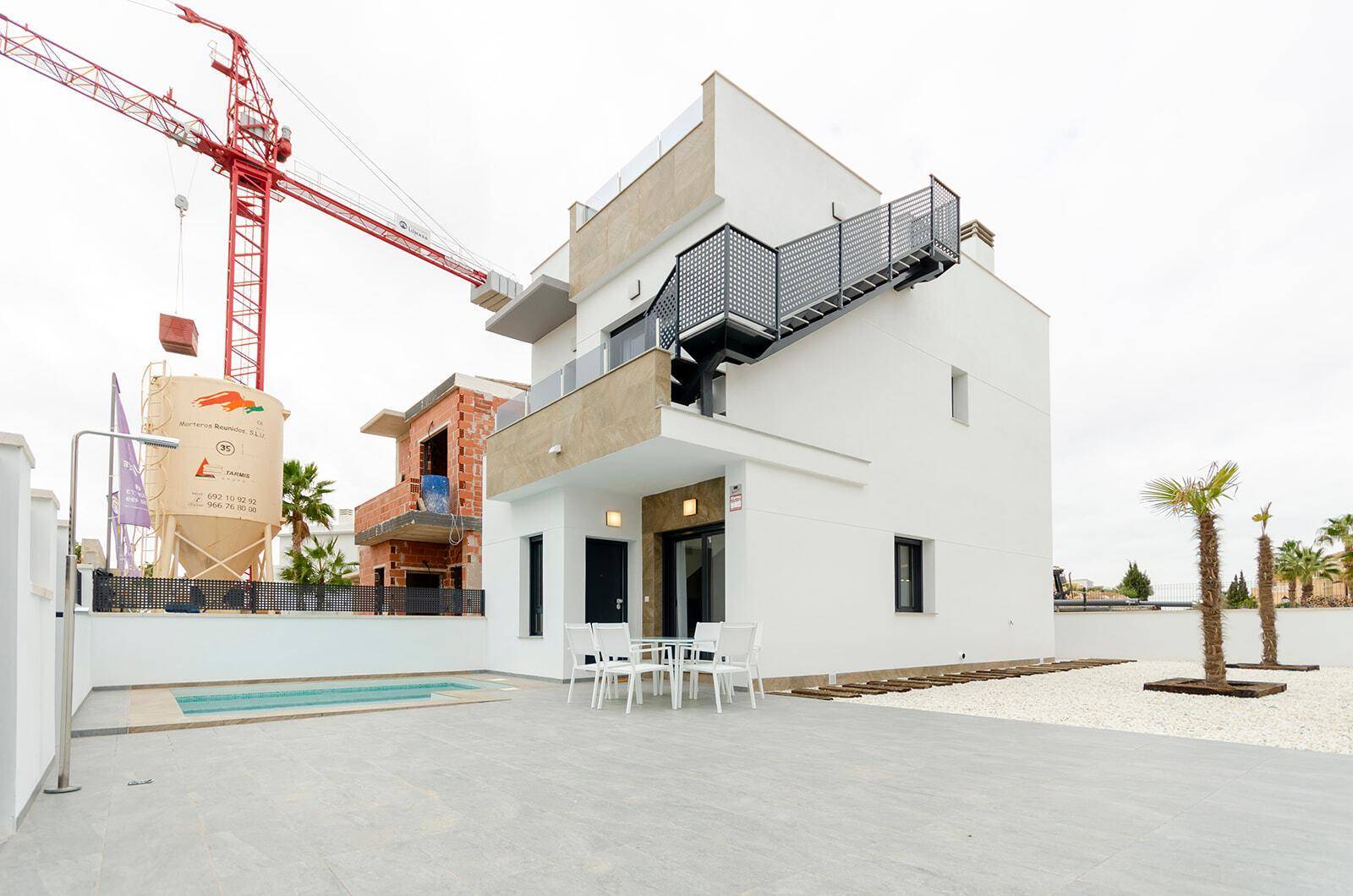 Moderne Villa mit privatem Pool und Außenbereich, umgeben von einer Baustelle und Palmen.