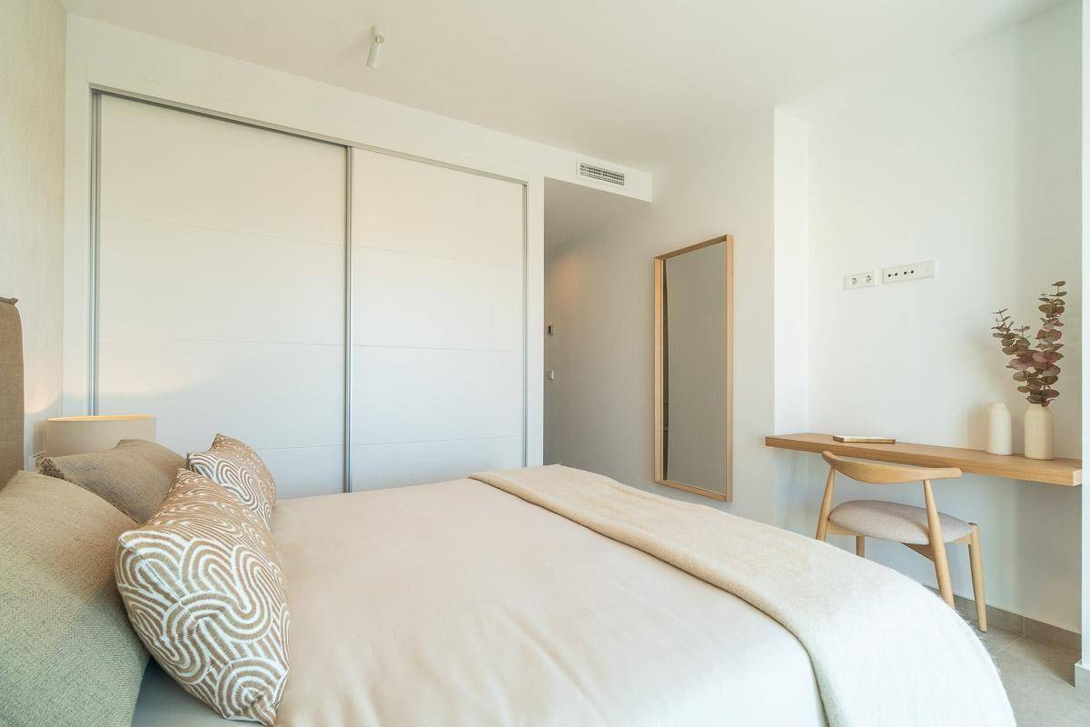 Modernes Schlafzimmer mit Doppelbett, Einbauschrank und einem kleinen Schreibtischbereich mit Spiegel.