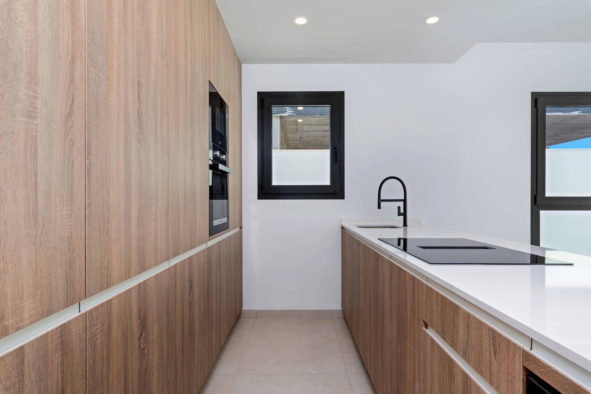 Moderne Küche mit Holzfronten, integriertem Backofen, Induktionskochfeld und weißer Arbeitsplatte.