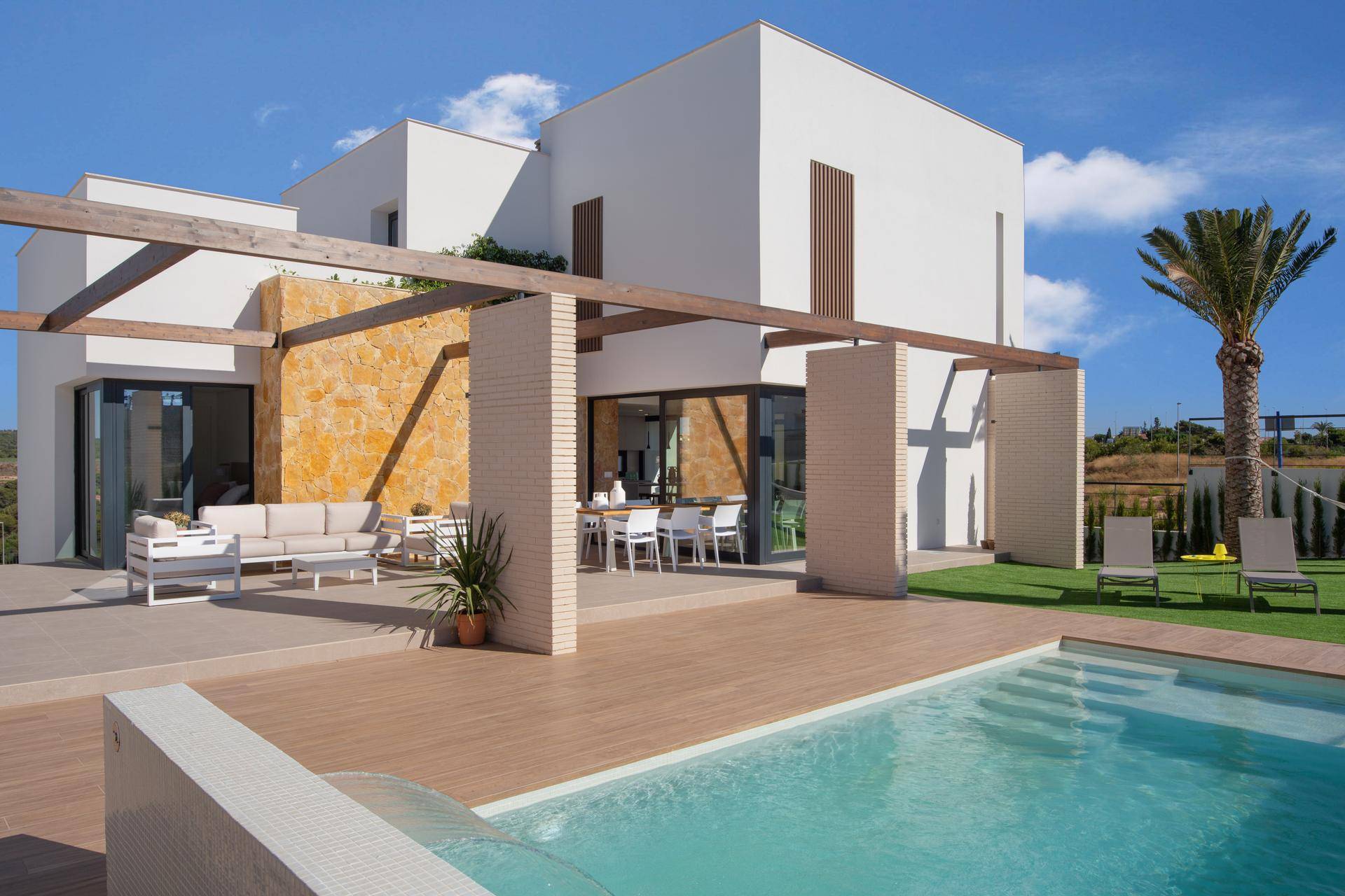 Weitläufige Außenanlage der modernen Villa mit Pool, Holzterrasse und verschiedenen Sitzbereichen.