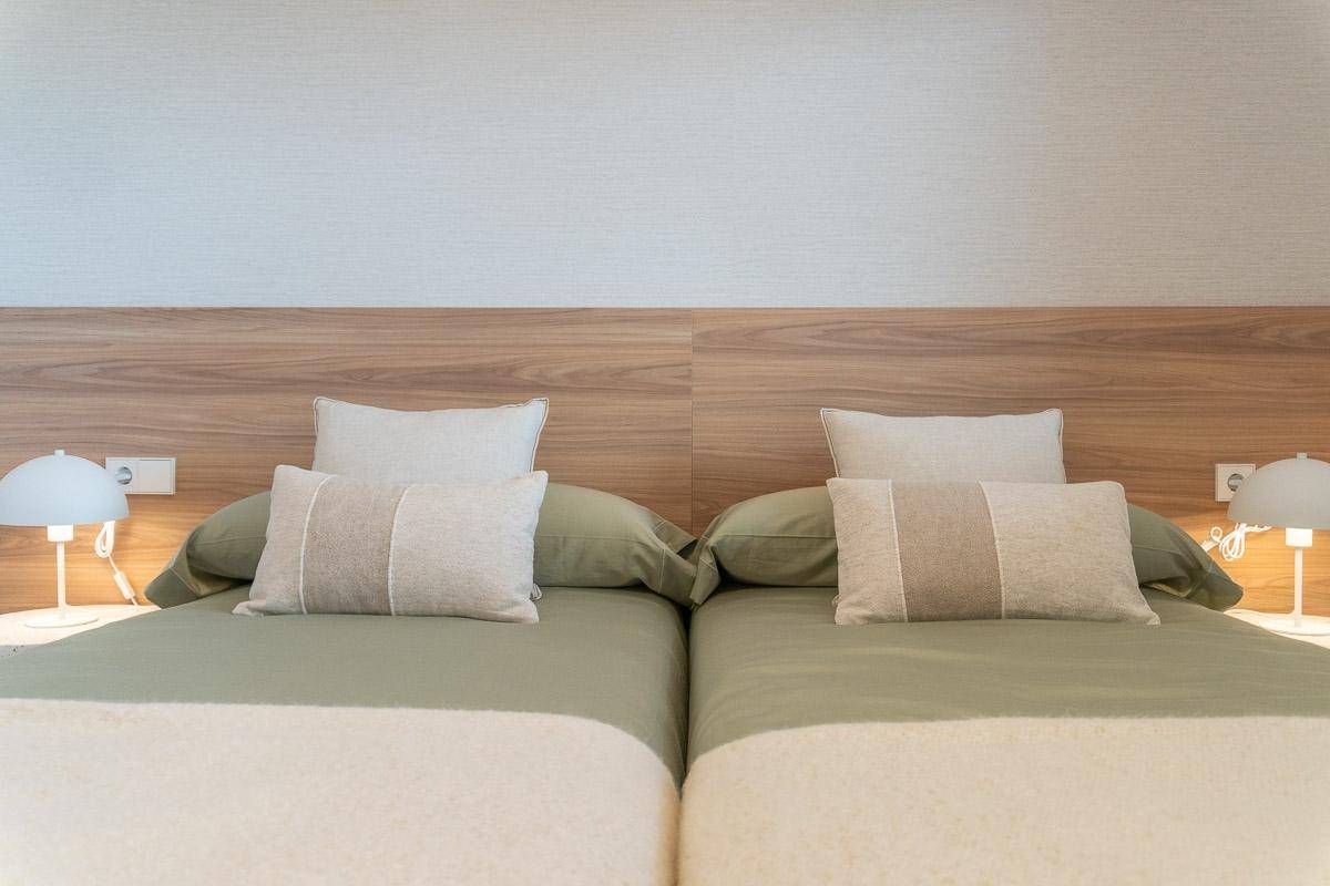 Detailansicht von zwei Einzelbetten mit Holz-Kopfteil und Nachttischlampen im Schlafzimmer.