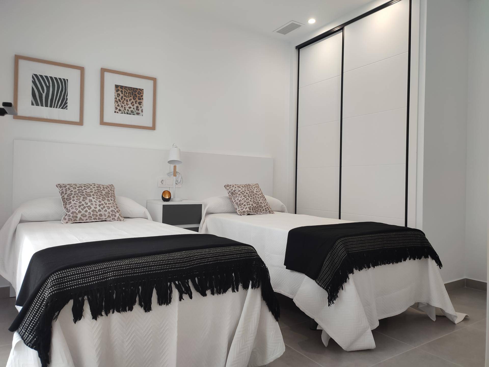Helles Schlafzimmer mit zwei Einzelbetten, modernen Nachttischen und integriertem Kleiderschrank.