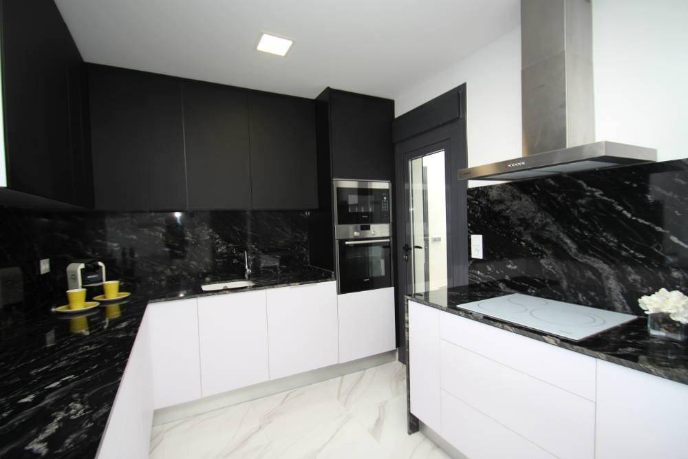 Moderne Küche mit schwarzer Granit-Arbeitsplatte, weißen Unterschränken und Induktionskochfeld.