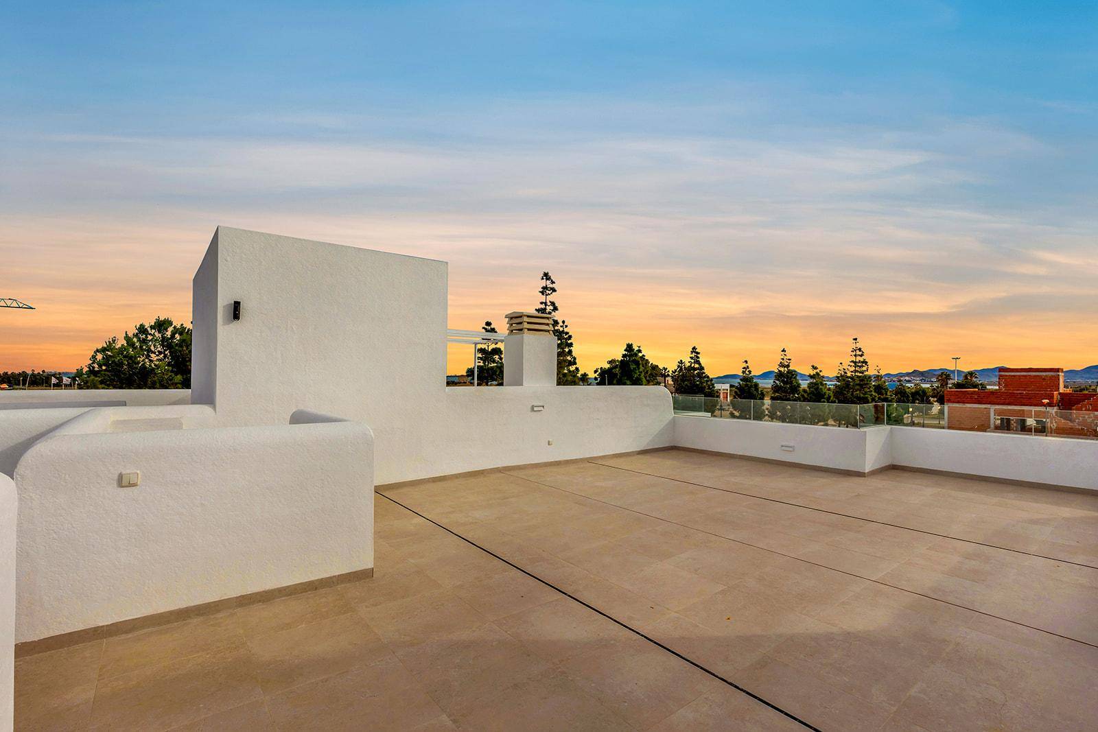 Geräumige Dachterrasse mit Fliesenboden und Blick auf den Sonnenuntergang.