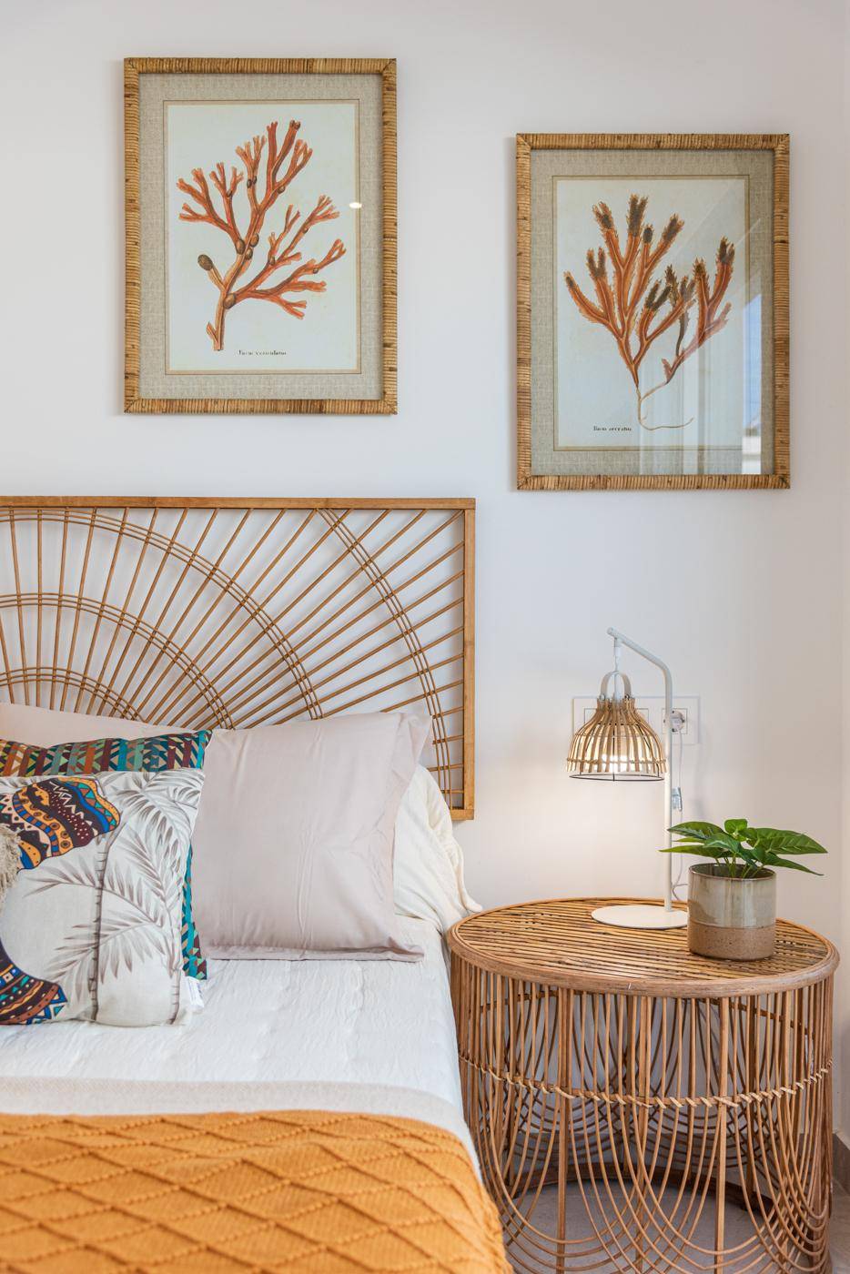 Schlafzimmer mit Rattan-Kopfteil, passendem Nachttisch und maritimen Bildern.