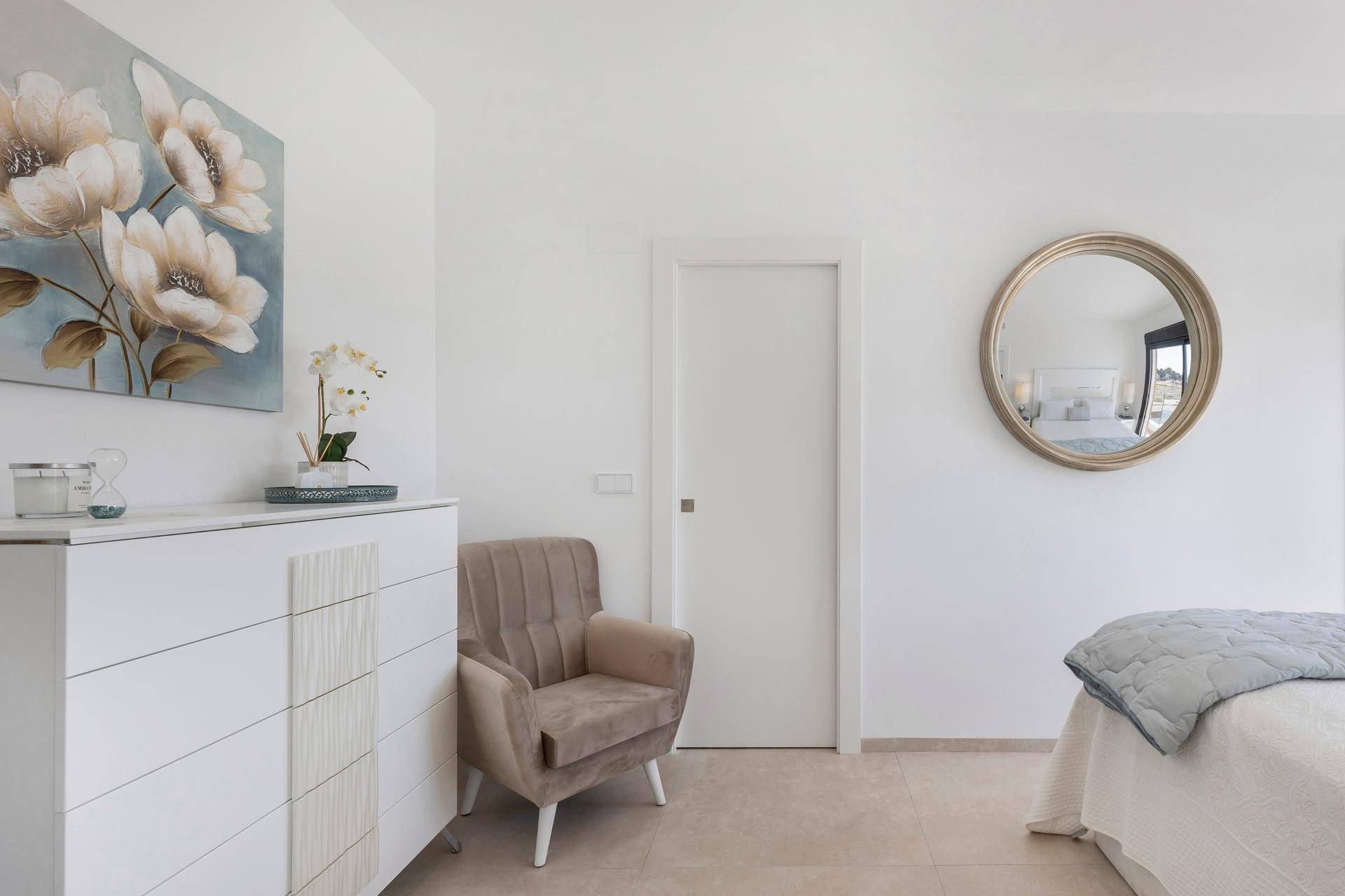 Schlafzimmer mit Kommode, rundem Spiegel und schlichter, eleganter Einrichtung.