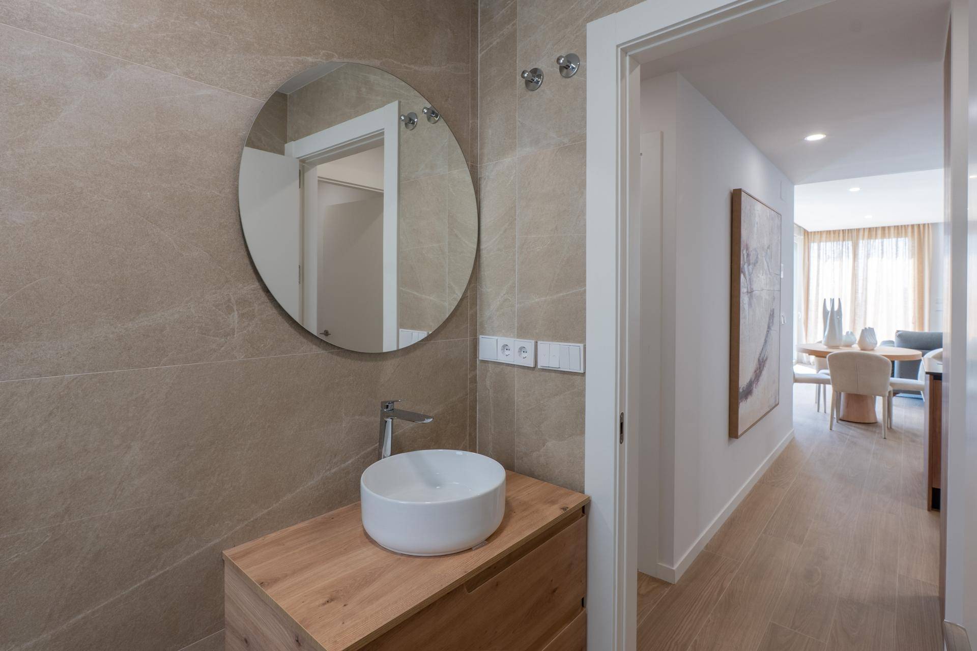 Modernes Badezimmer mit rundem Spiegel, Einzelwaschbecken und Holztisch.