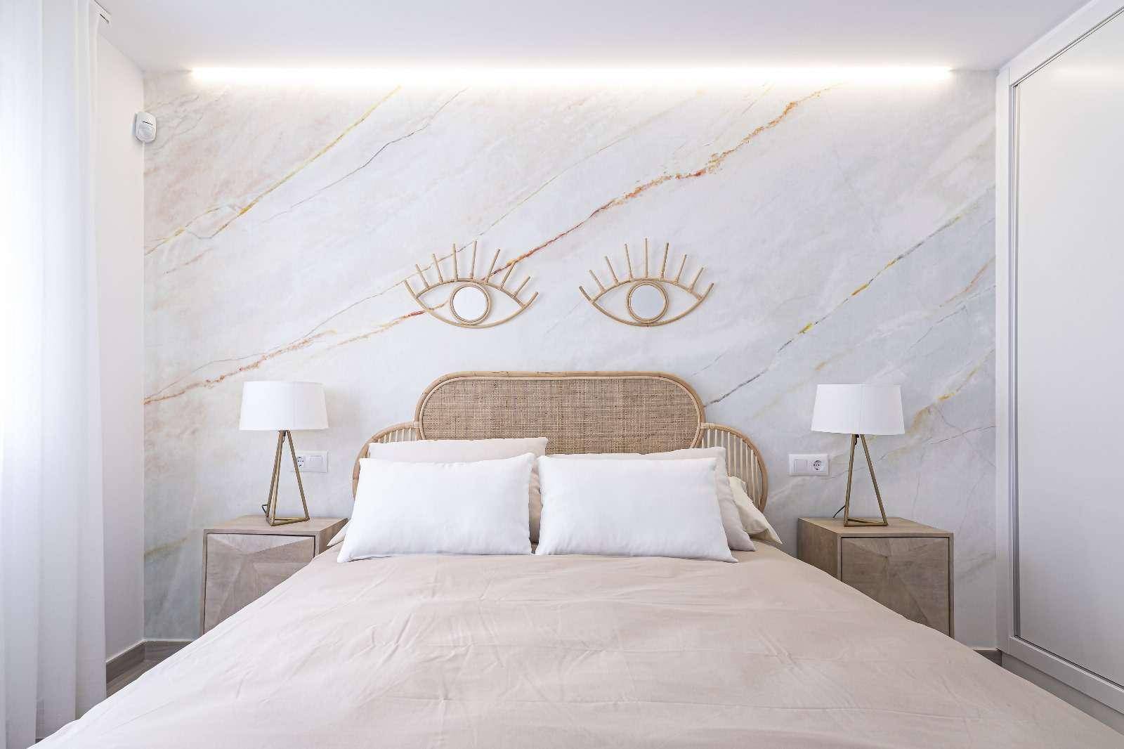 Helles Schlafzimmer mit modernem Bett, Nachttischen und dekorativer Marmorwand.