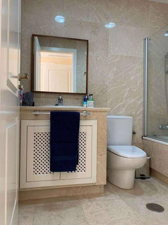 Badezimmer mit Waschbecken, Spiegel und Unterschrank, gefliest in hellem Marmoroptik.