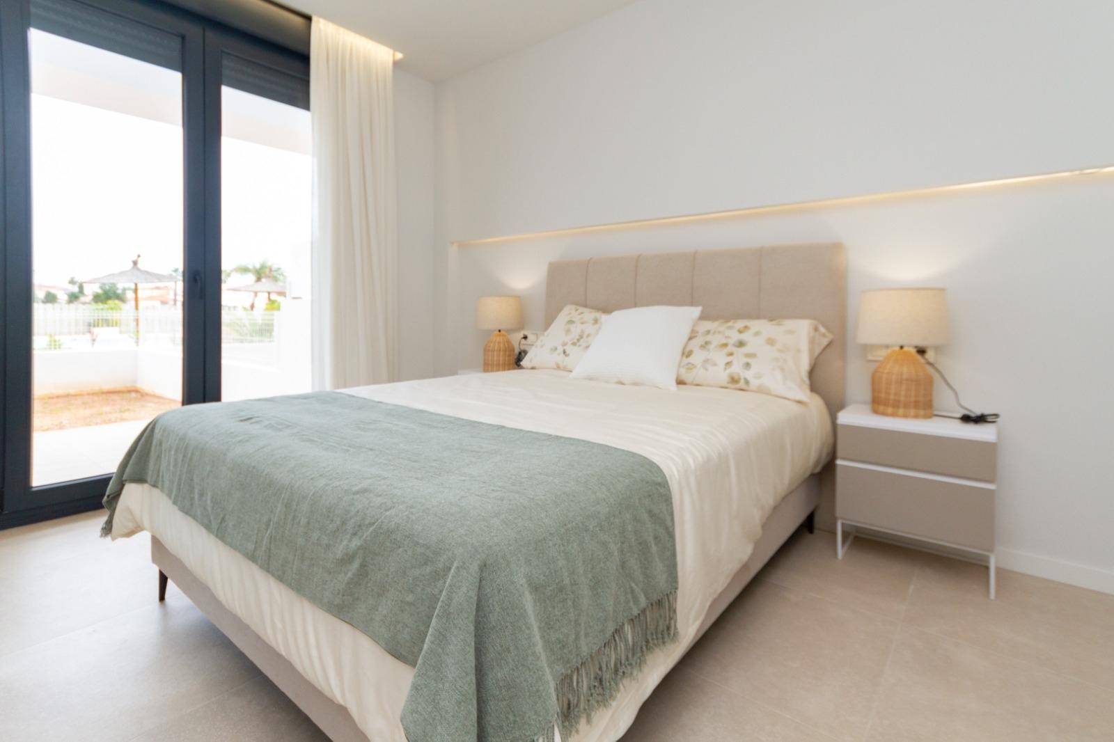 Helles Schlafzimmer mit Doppelbett, Nachttischen und direktem Zugang zu einem Außenbereich.