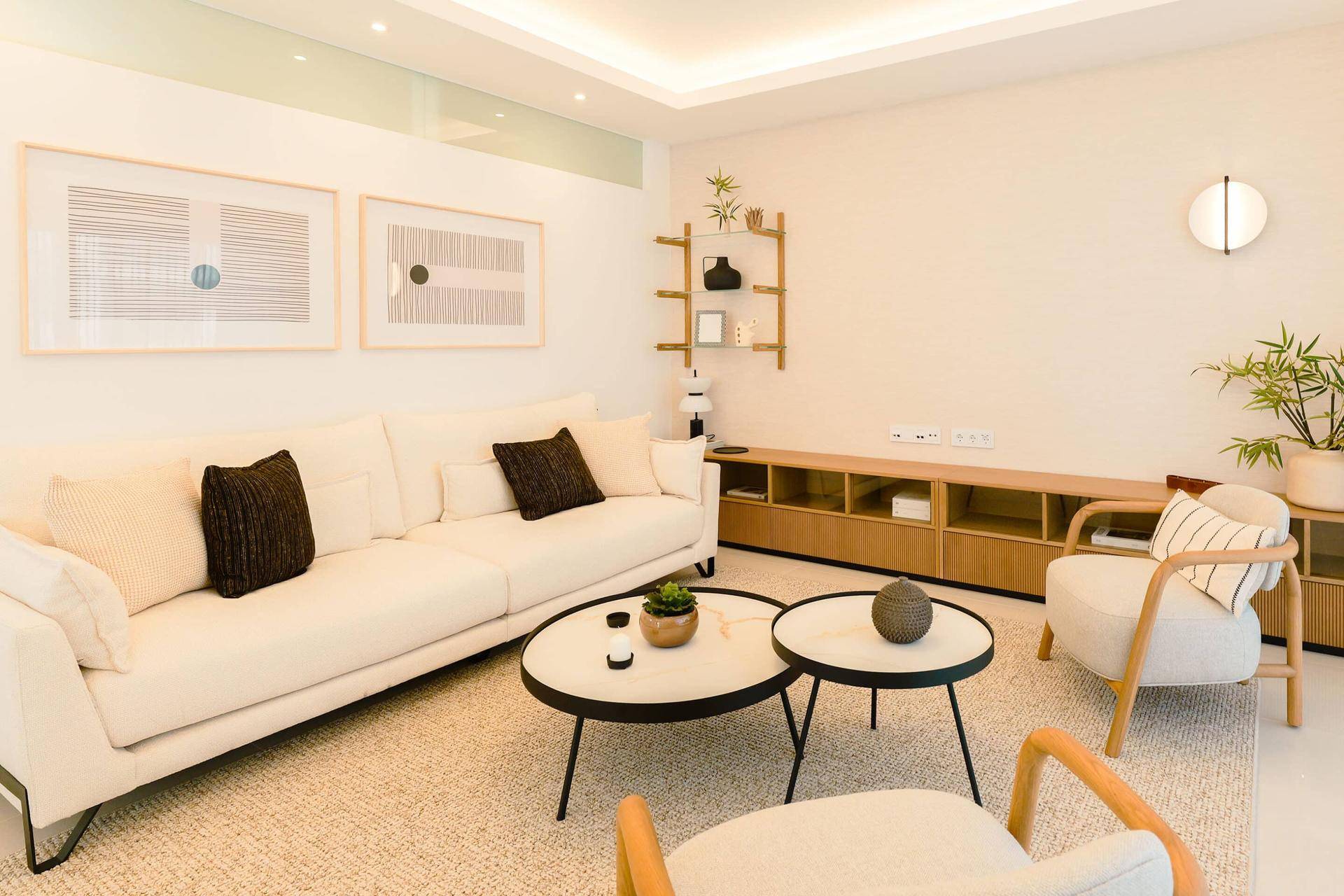 Heller Wohnbereich mit beigem Sofa, Couchtischen und moderner Wanddekoration.