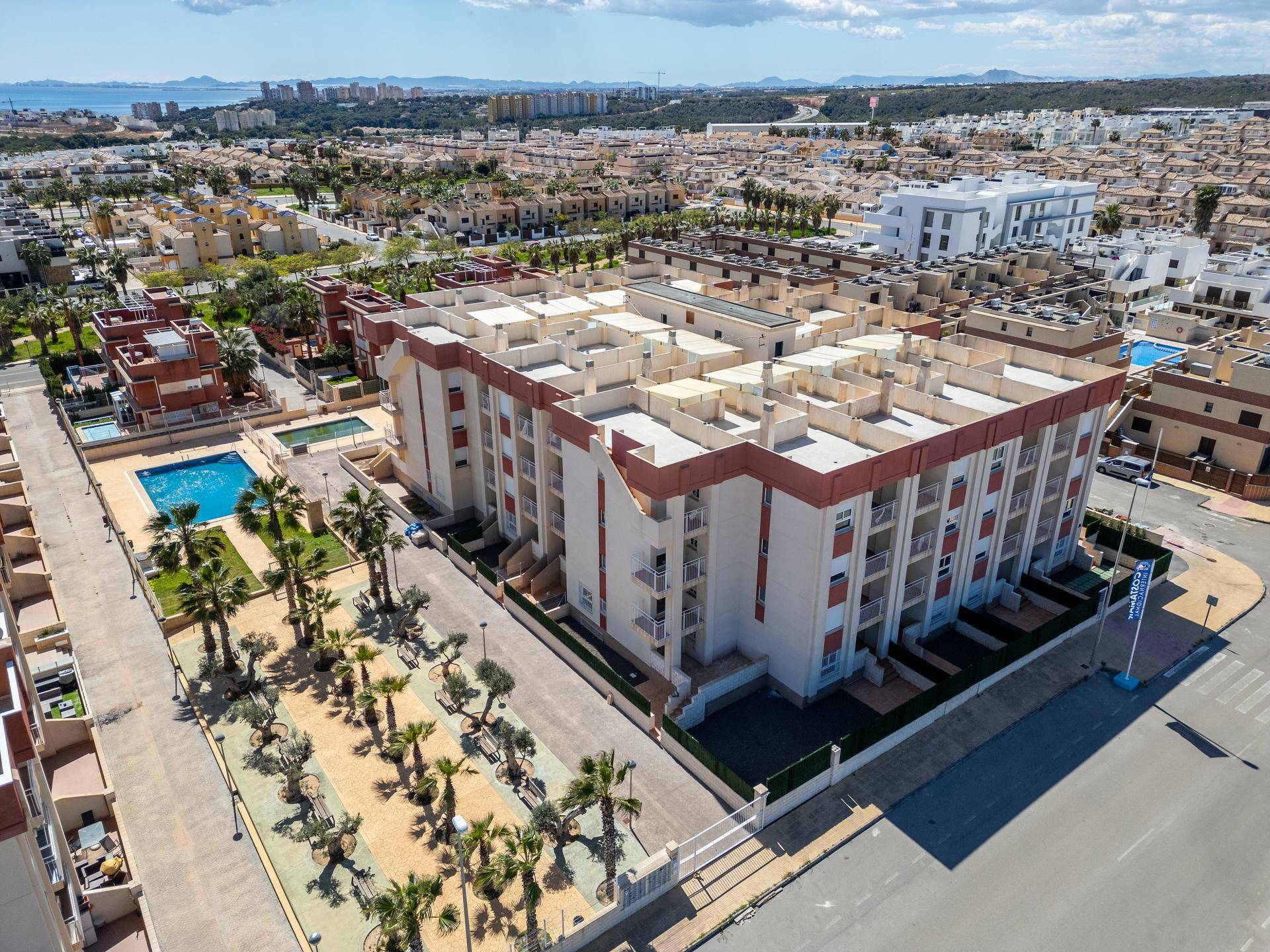 Weitläufige Luftaufnahme des Wohnkomplexes mit Gebäuden, Straßen und dem Mittelmeer in der Ferne.