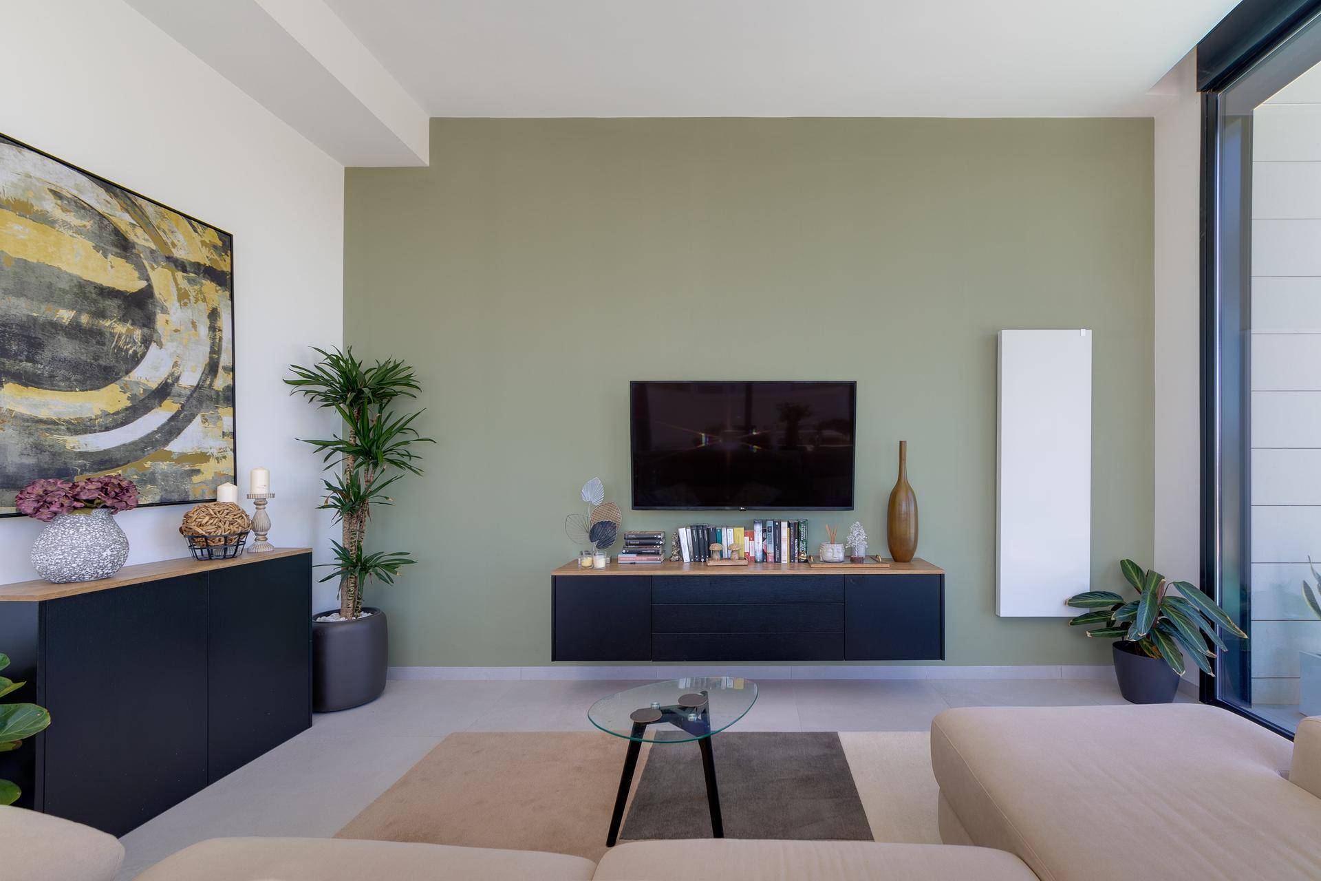 Heller Wohnbereich mit beigem Sofa, grüner Akzentwand und modernen Möbeln.
