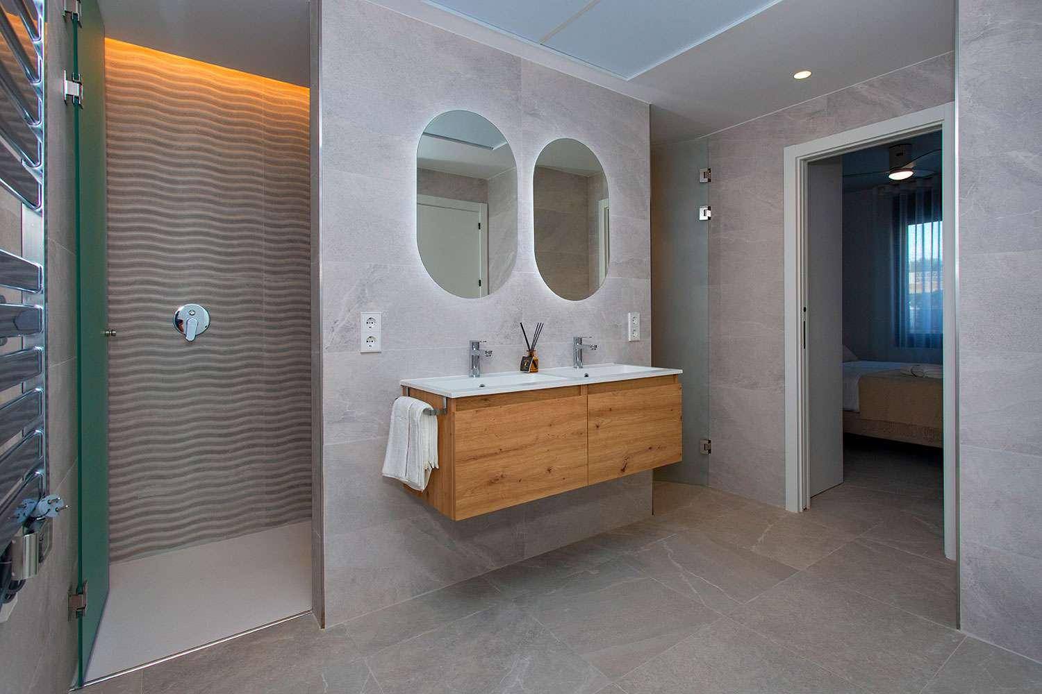 Luxuriöses Badezimmer mit Doppelwaschbecken, begehbarer Dusche und beheiztem Handtuchhalter.