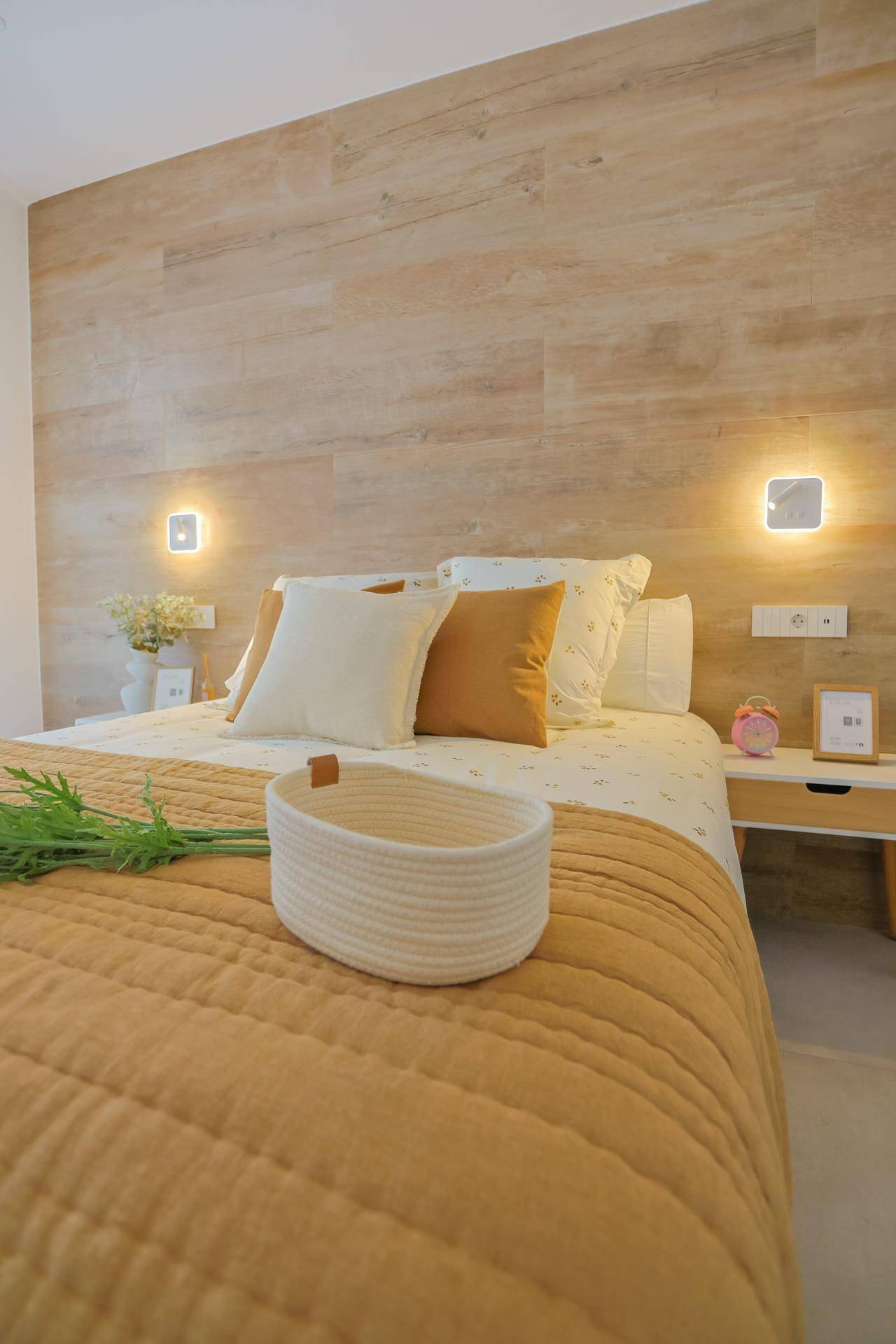 Helles Schlafzimmer mit Holzwand als Kopfteil, gemütlichem Bett und indirekter Beleuchtung.
