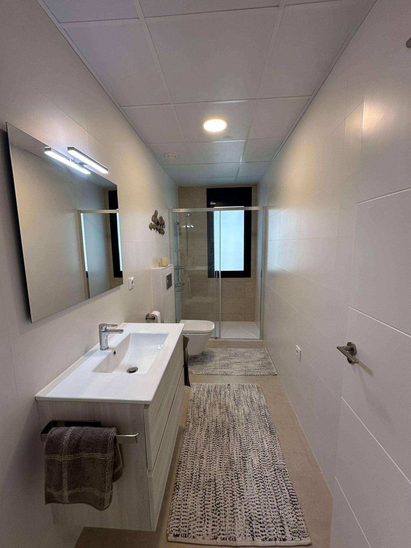 Langes, modernes Badezimmer mit Einzelwaschbecken, Dusche und Fenster.