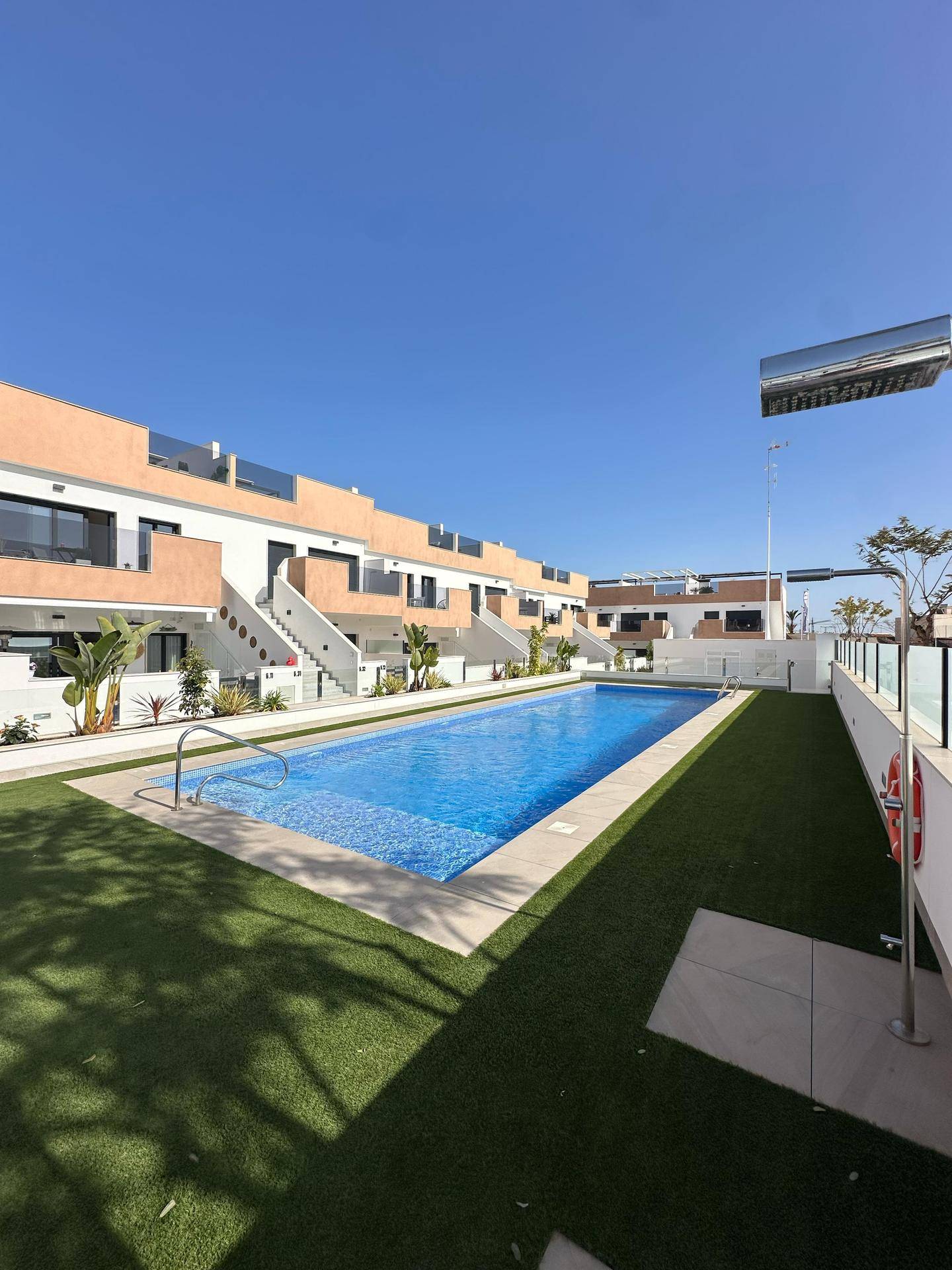Gepflegter Gemeinschaftspool mit Außendusche und Sicherheitsausrüstung in sonniger Umgebung.