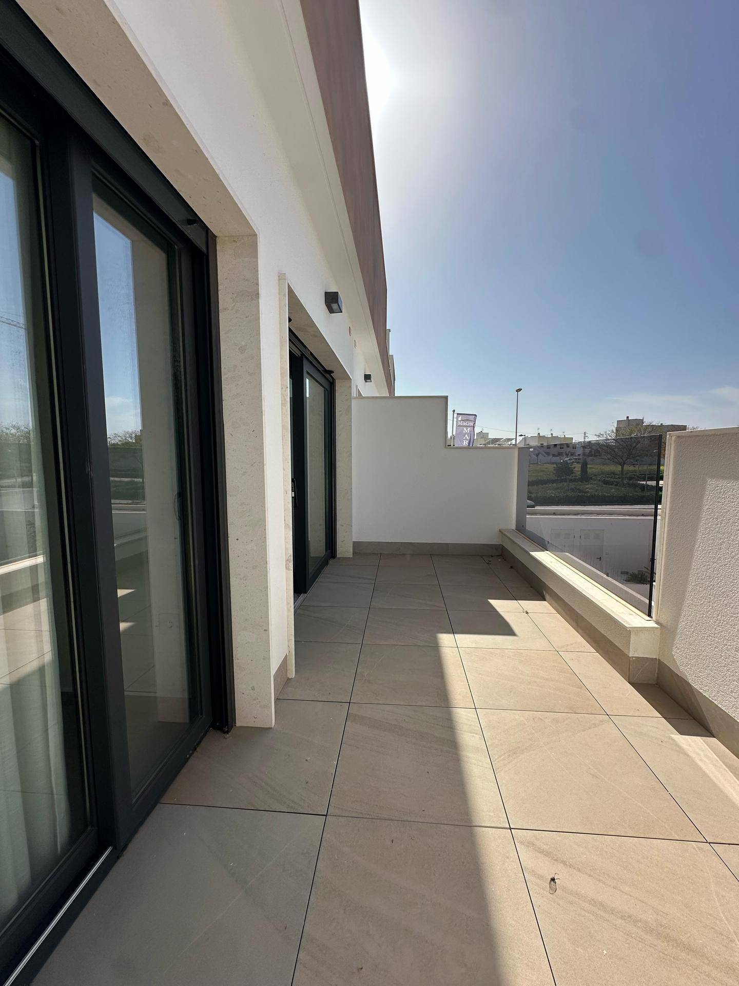 Geräumige, geflieste Terrasse mit Glasgeländer und viel Sonnenlicht, ideal zum Entspannen.