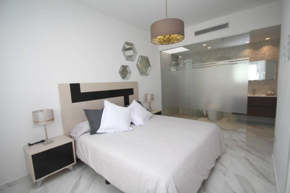Helles Schlafzimmer mit Doppelbett, Nachttisch und offenem Zugang zum modernen Bad.