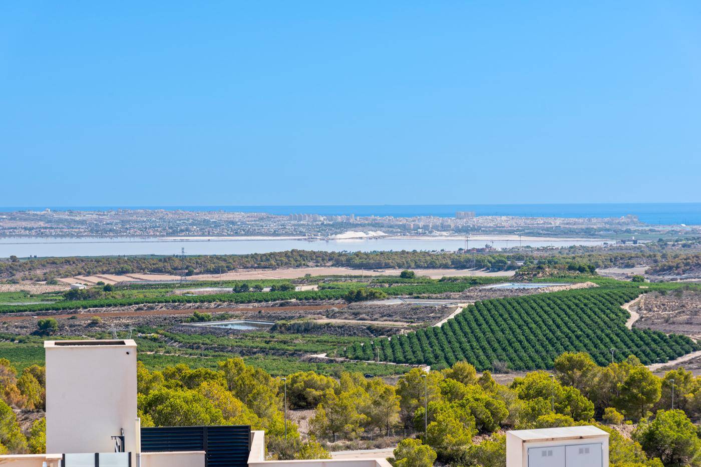 Weitblick über grüne Felder und das Meer mit einer Küstenstadt am Horizont.