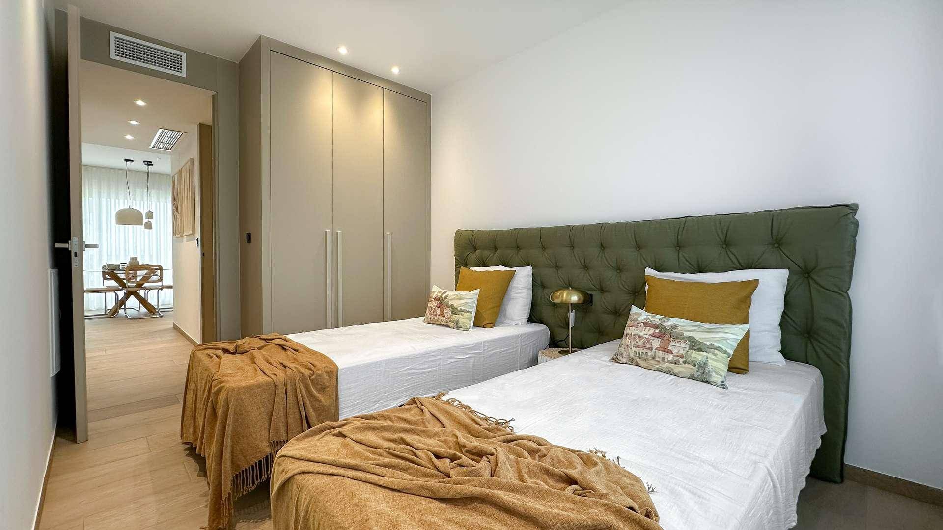 Helles Schlafzimmer mit zwei Einzelbetten, gepolstertem Kopfteil und Einbauschränken.