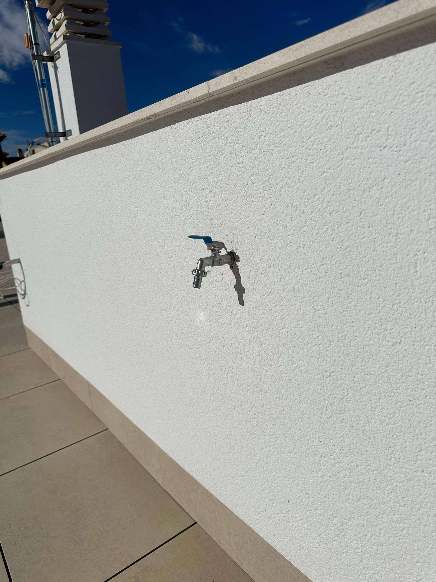 Wasserhahn an der weißen Außenwand auf der Dachterrasse für Bewässerung oder Reinigung.