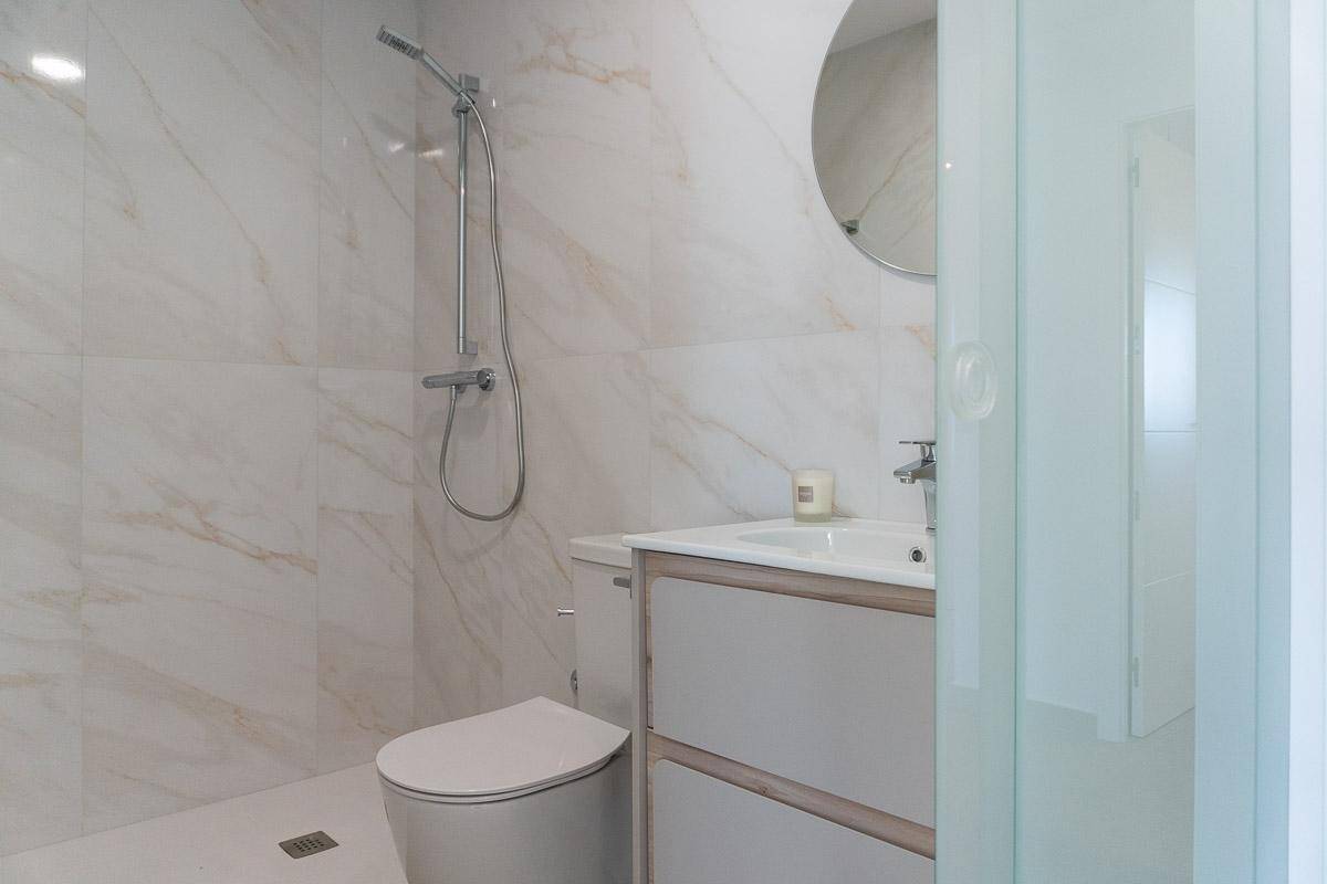 Helles Badezimmer mit Marmoroptik-Fliesen, moderner Dusche und Waschtisch mit Spiegel.