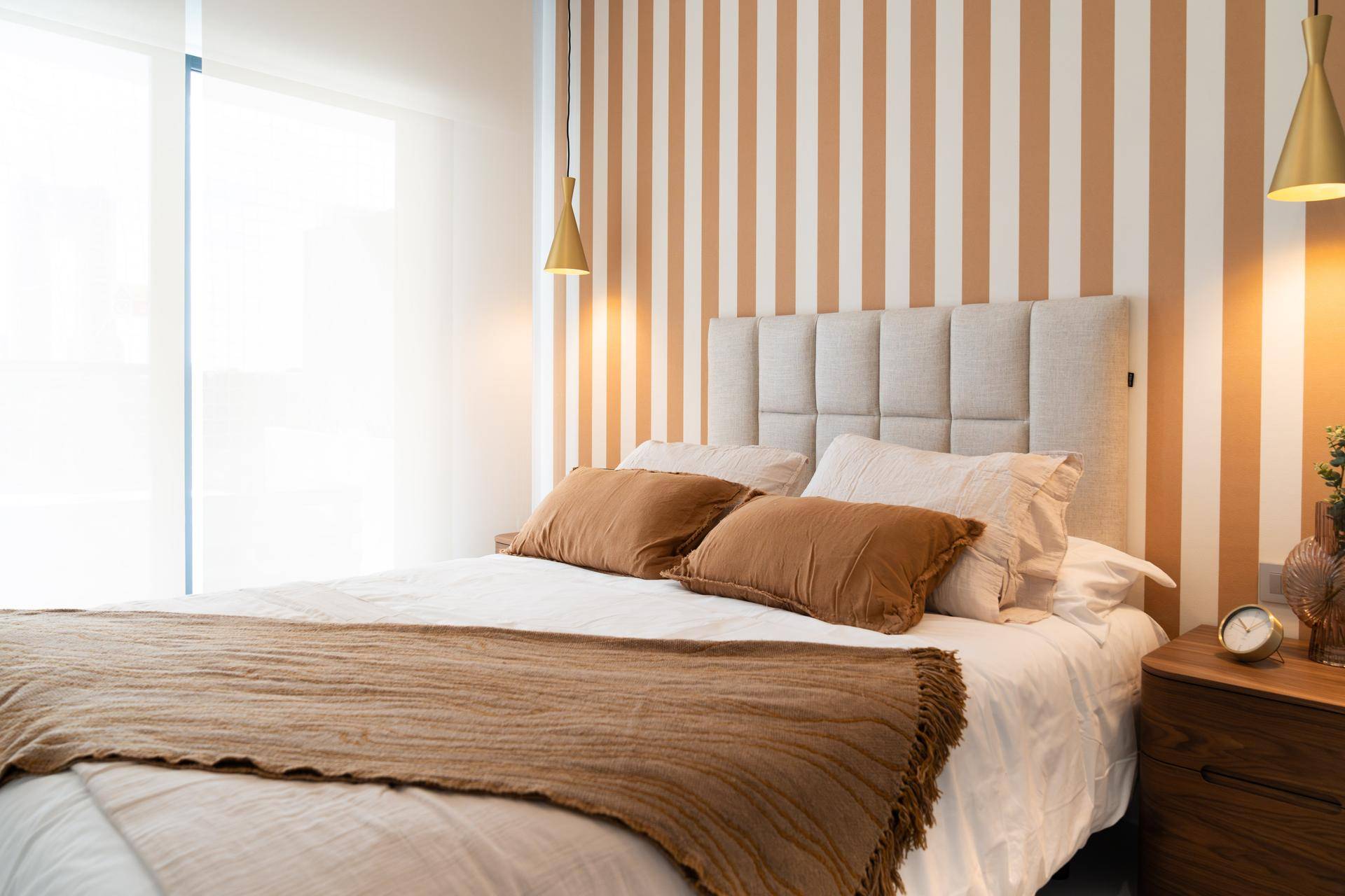 Gemütliches Schlafzimmer mit Doppelbett, gestreifter Akzentwand und stilvollen Pendelleuchten.