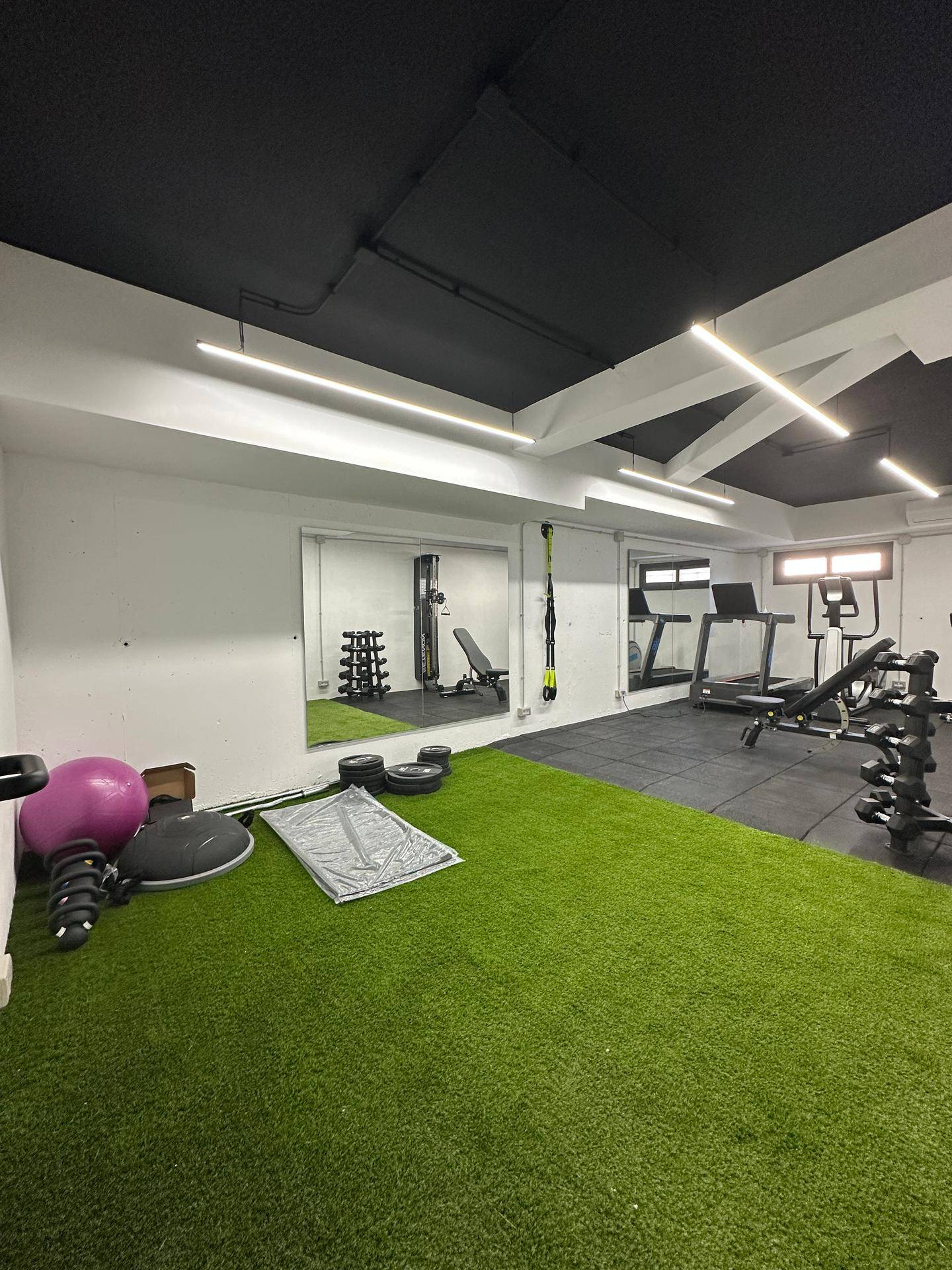 Fitnessraum mit Hanteln, Trainingsmatten und großem Spiegel für Übungen.