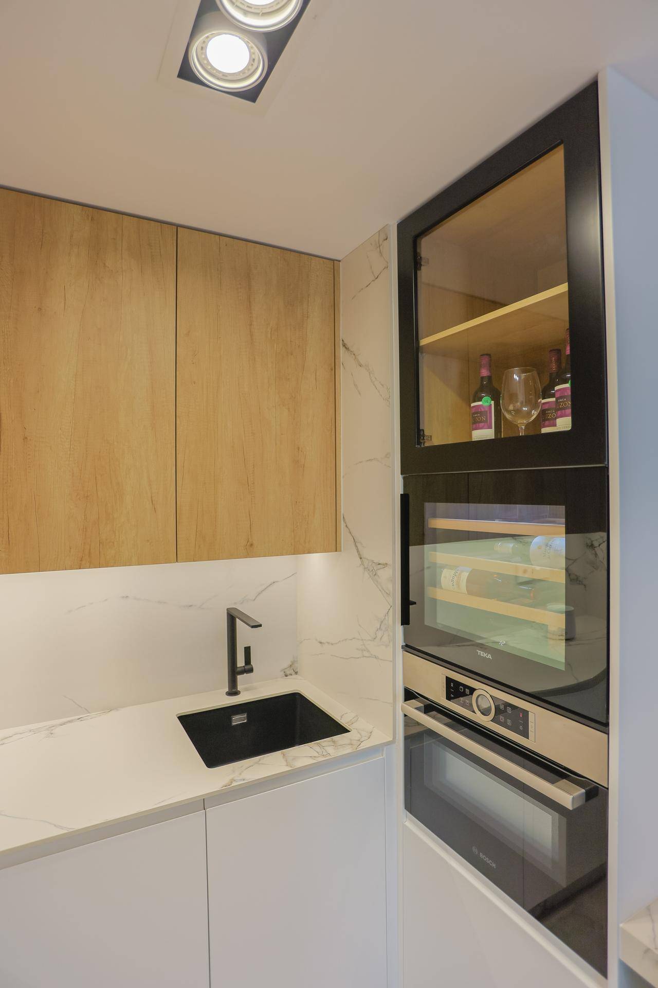 Moderne Küche mit weißen und holzfarbenen Schränken, schwarzer Spüle und integrierten Geräten.