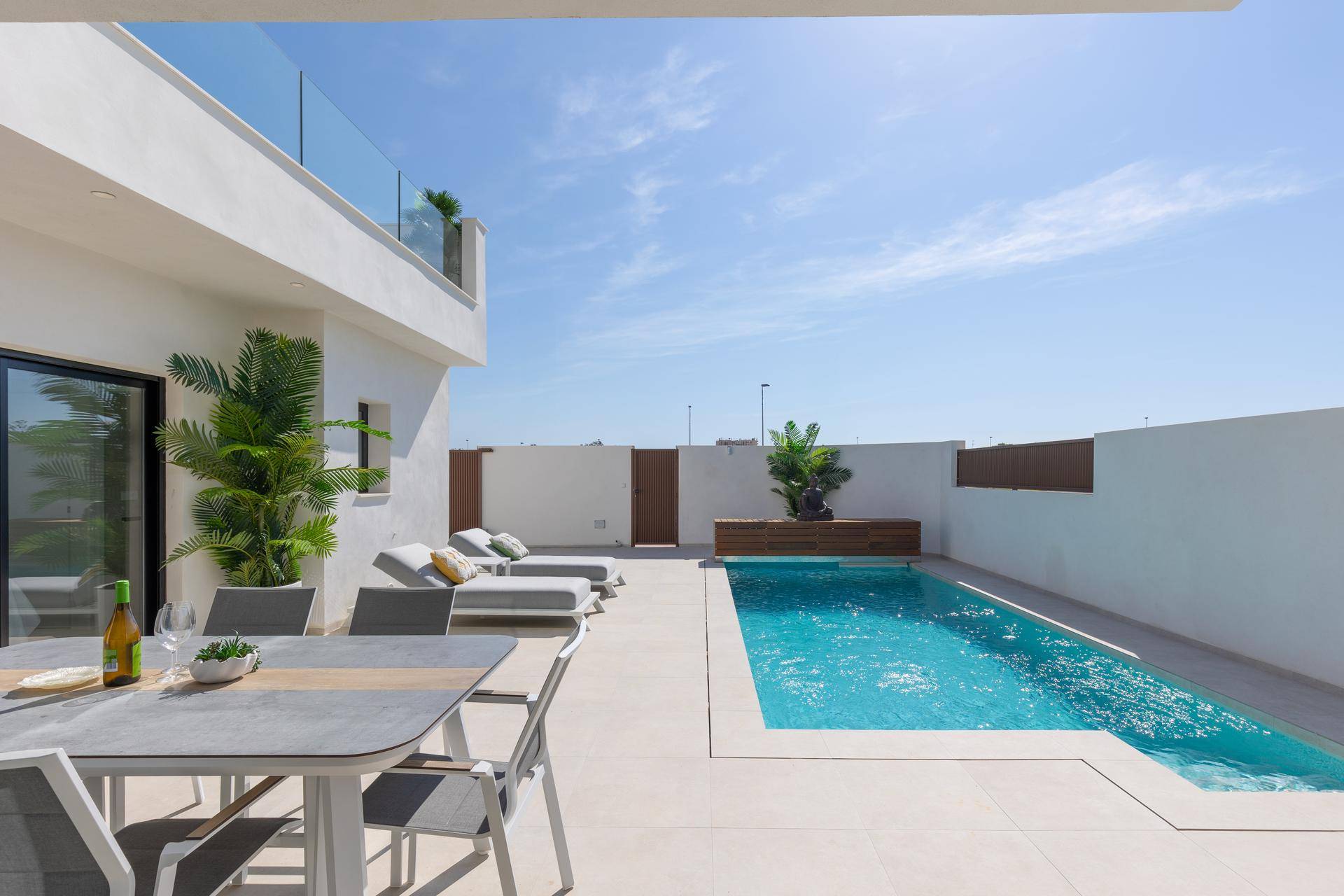 Geräumige Terrasse mit Pool, Essbereich und Liegestühlen unter blauem Himmel.