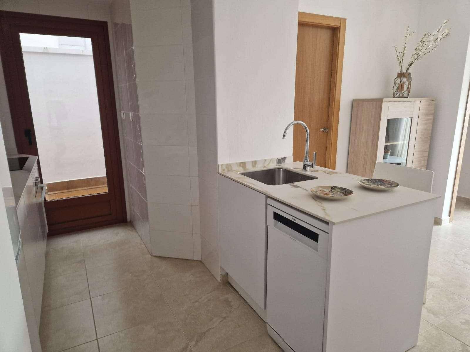 Moderne Küchenzeile mit weißer Arbeitsplatte, Spüle und integriertem Geschirrspüler, daneben eine Tür.