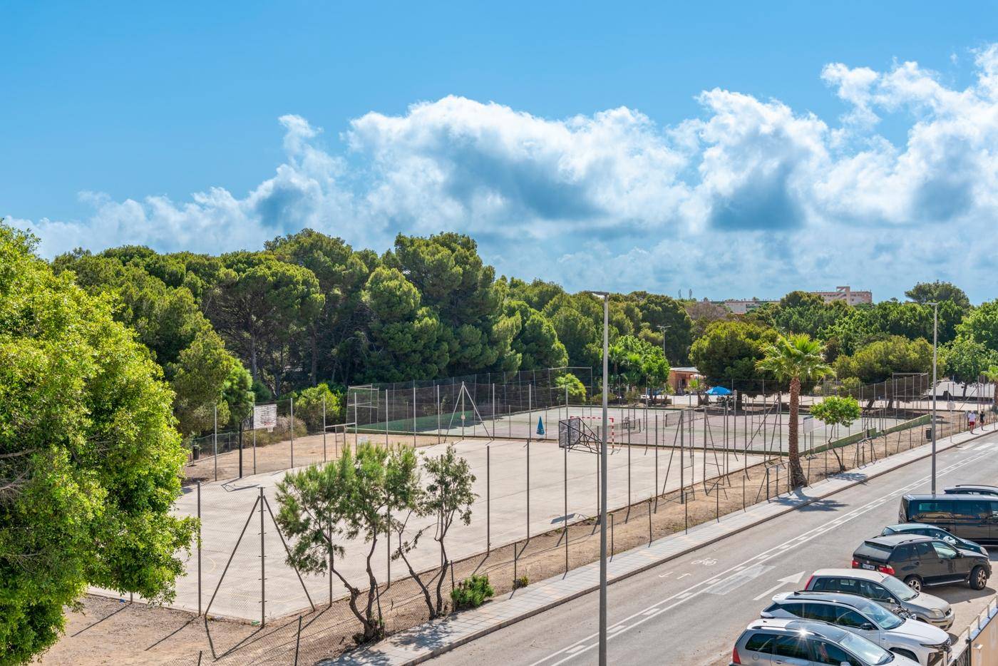 Weitläufiger Blick auf Sportanlagen und eine Straße mit parkenden Autos.