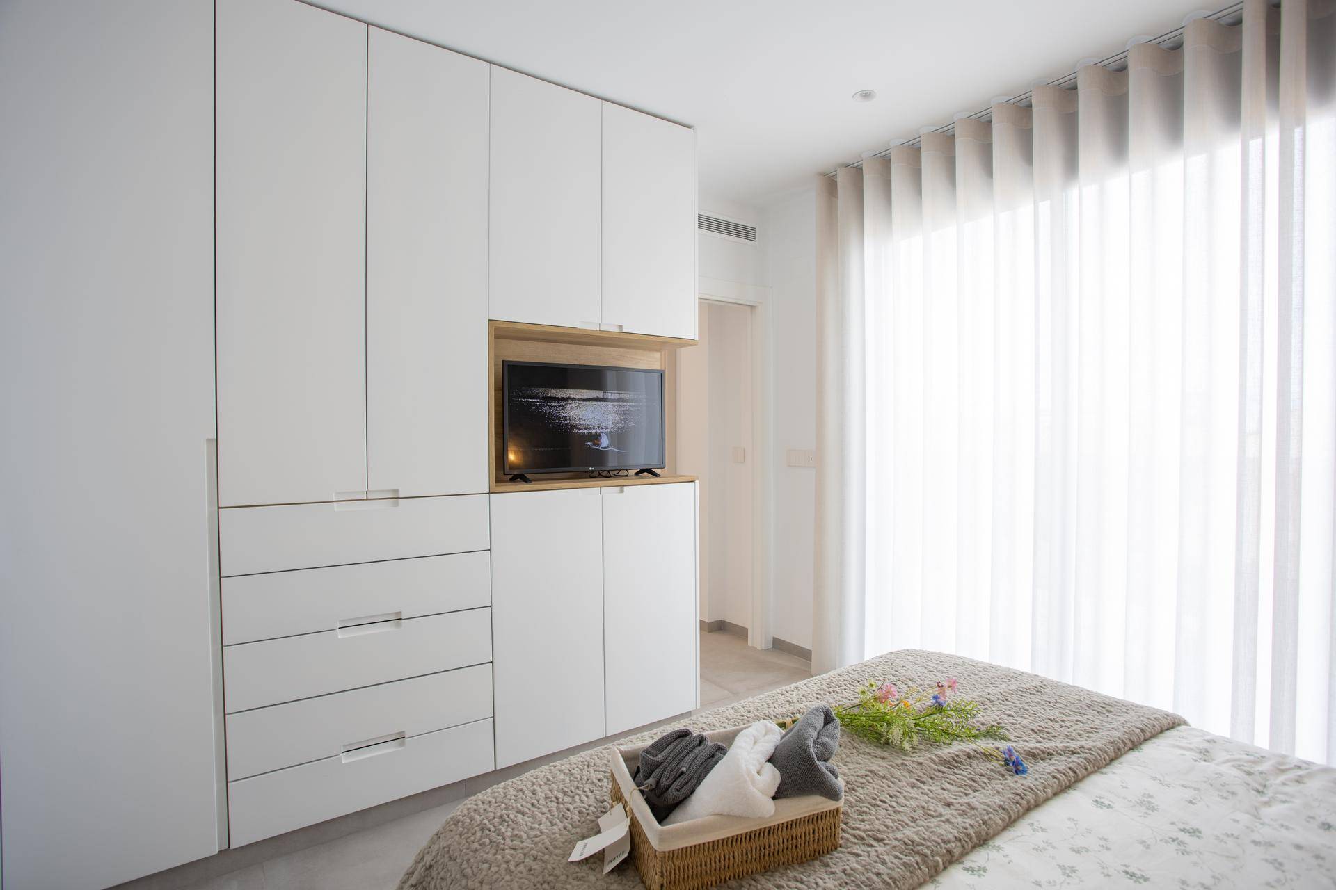 Schlafzimmer mit großen Einbauschränken, integriertem Fernseher und viel Tageslicht.