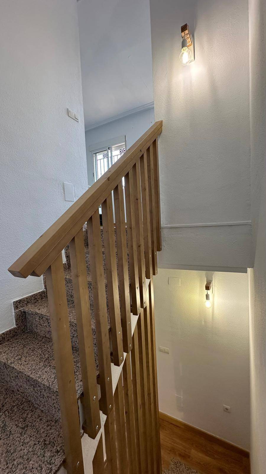 Treppenhaus mit Holzgeländer und Wandleuchten, die den Weg beleuchten.