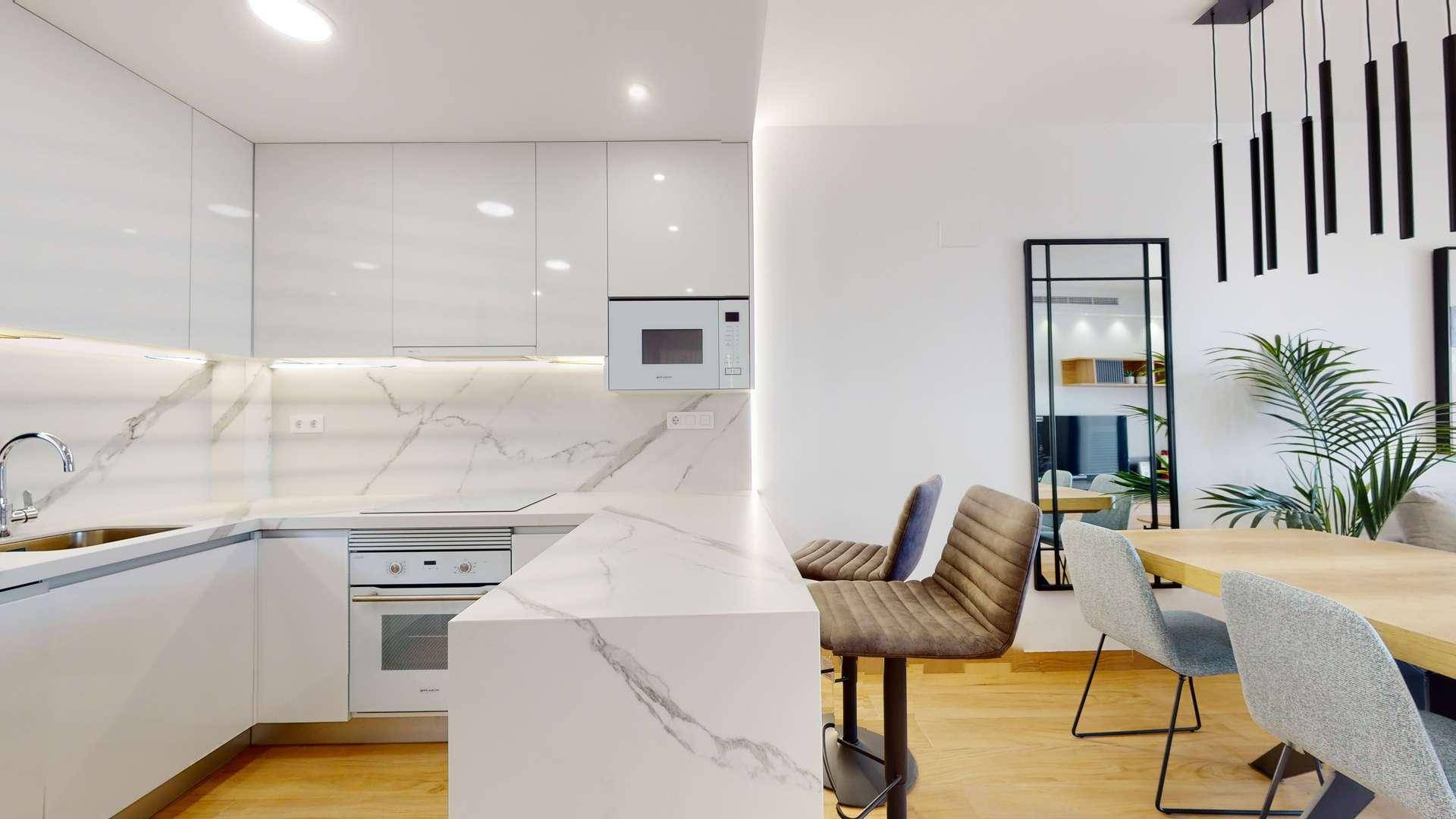 Moderne weiße Küche mit Marmor-Arbeitsplatten, integrierter Mikrowelle und Frühstücksbar.