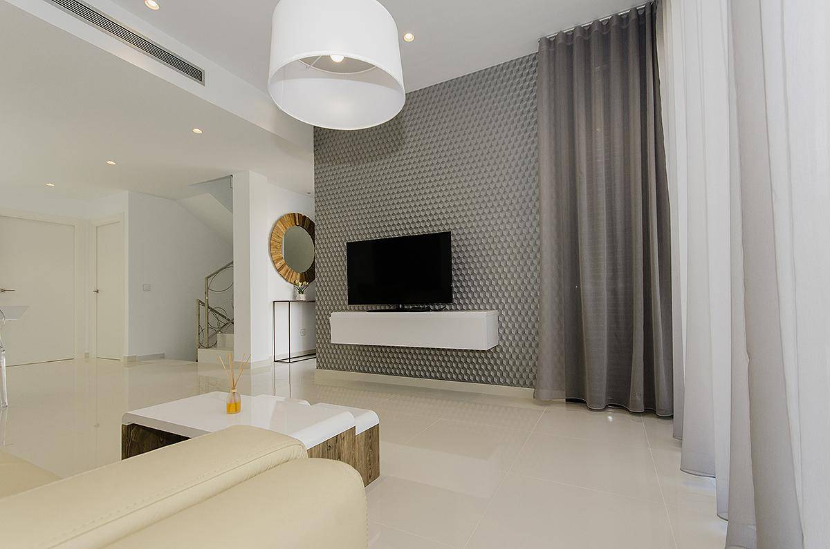 Stilvolles Wohnzimmer mit Wandfernseher, grauer Akzentwand und großen Fenstern.
