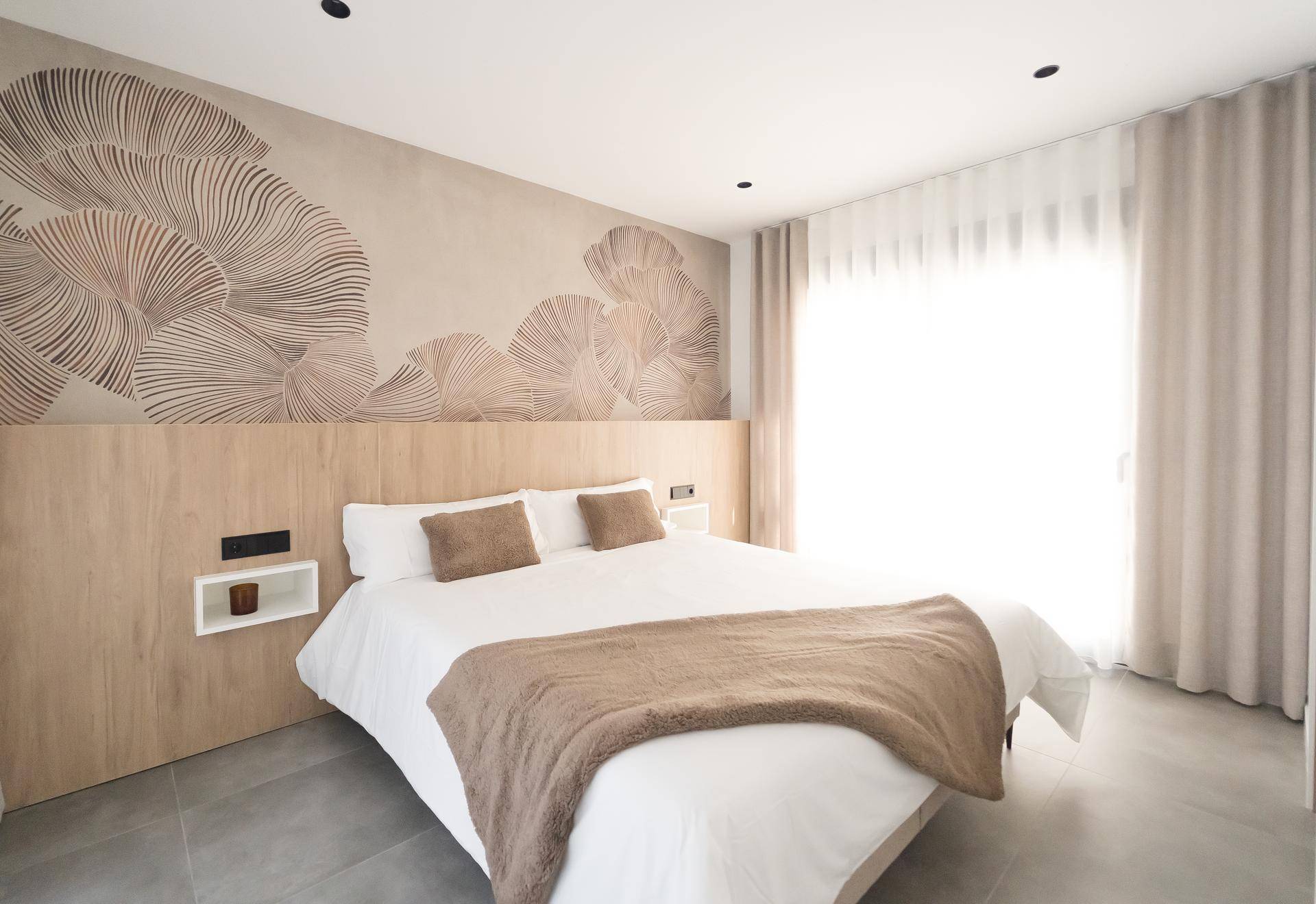 Helles Schlafzimmer mit Doppelbett, Holzkopfteil und dekorativer Wandgestaltung.