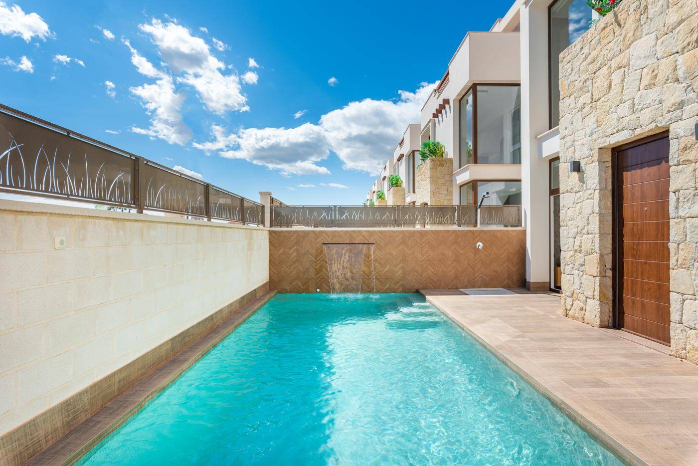 Langer, schmaler Pool mit integriertem Wasserfall und gefliester Terrasse, umgeben von einer Mauer.