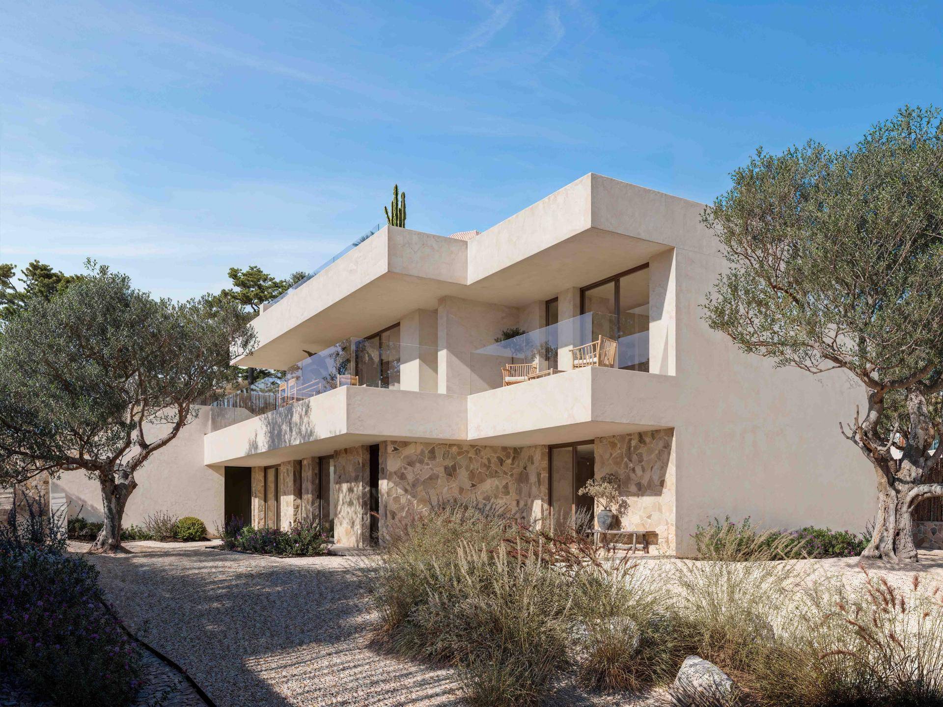 Moderne Villa mit Natursteinelementen und großen Fensterfronten, umgeben von mediterraner Vegetation.