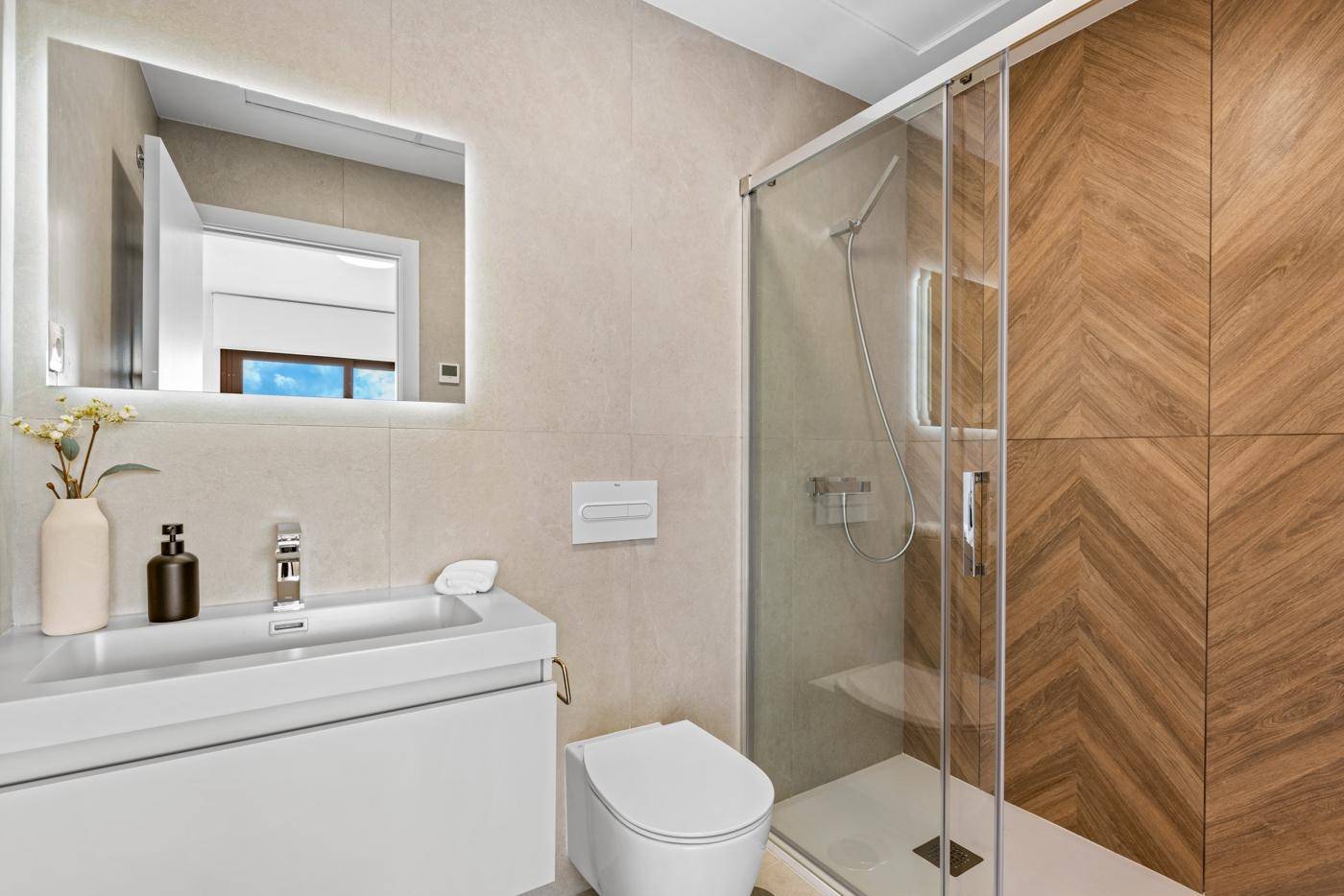 Stilvolles Badezimmer mit Duschkabine, Waschtisch und beleuchtetem Wandspiegel.