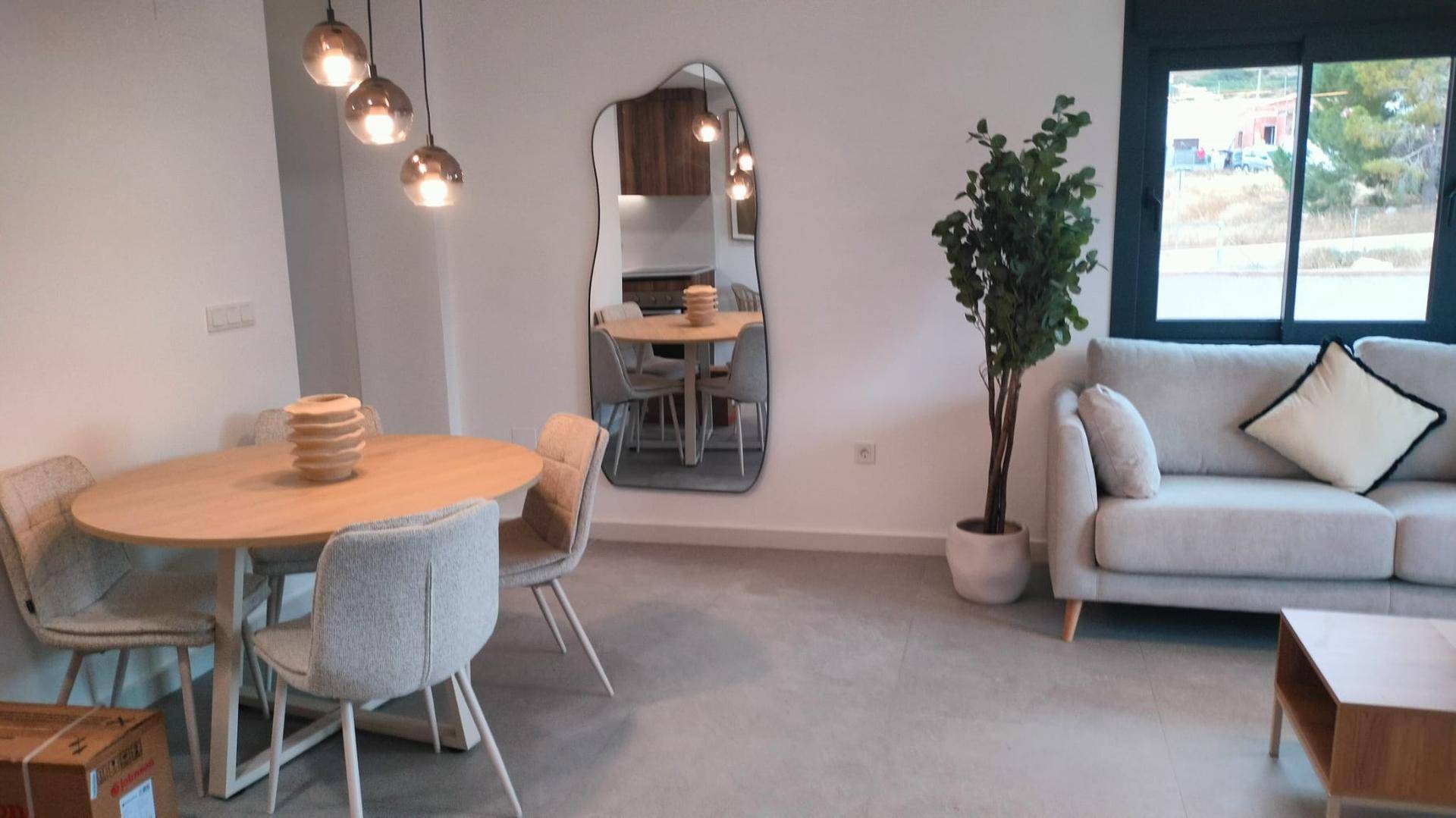 Heller Wohn-Essbereich mit rundem Holztisch, Sofa und großem Spiegel.