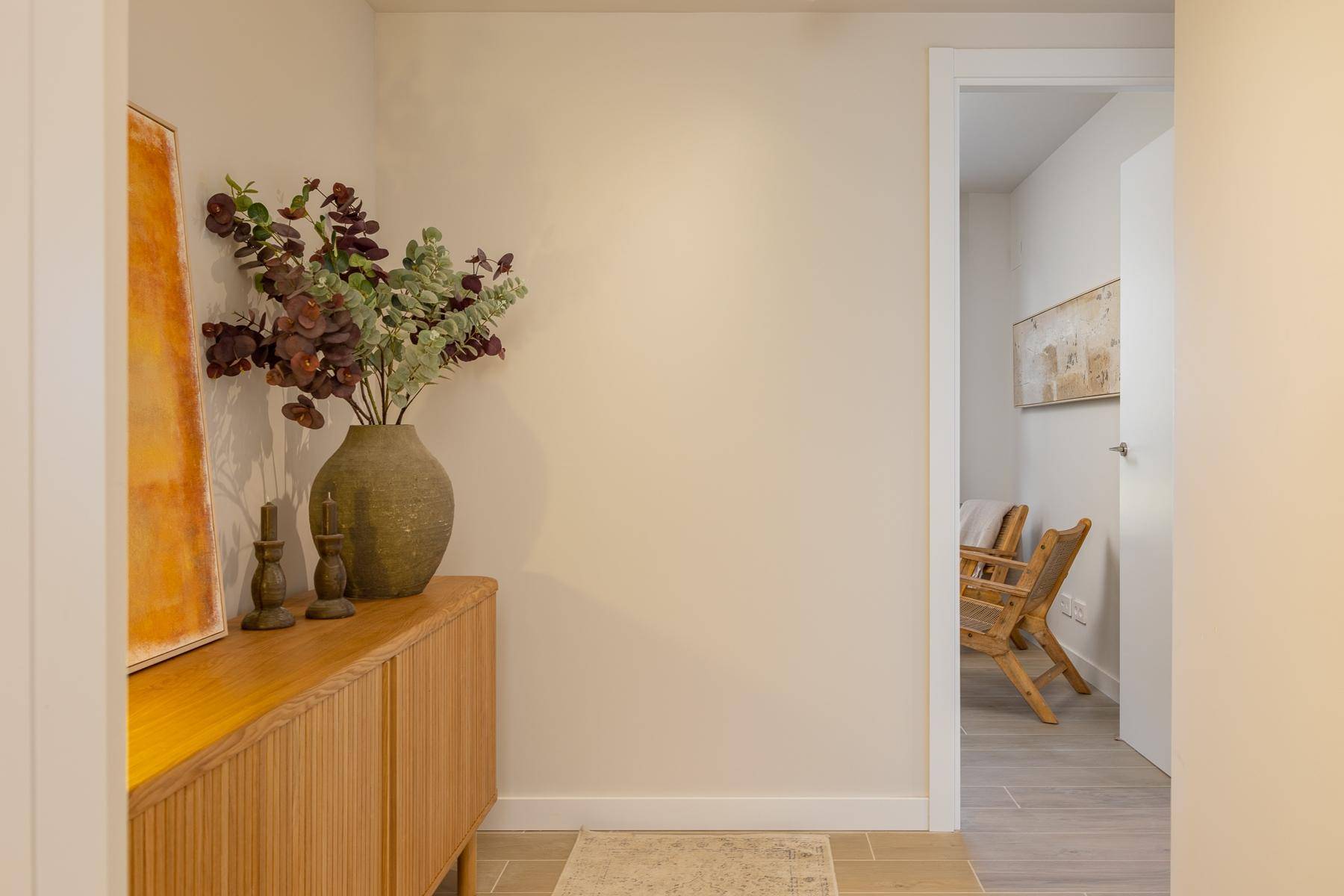 Detailansicht eines modernen Holzschranks mit Vase und Kerzen im hellen Flur.