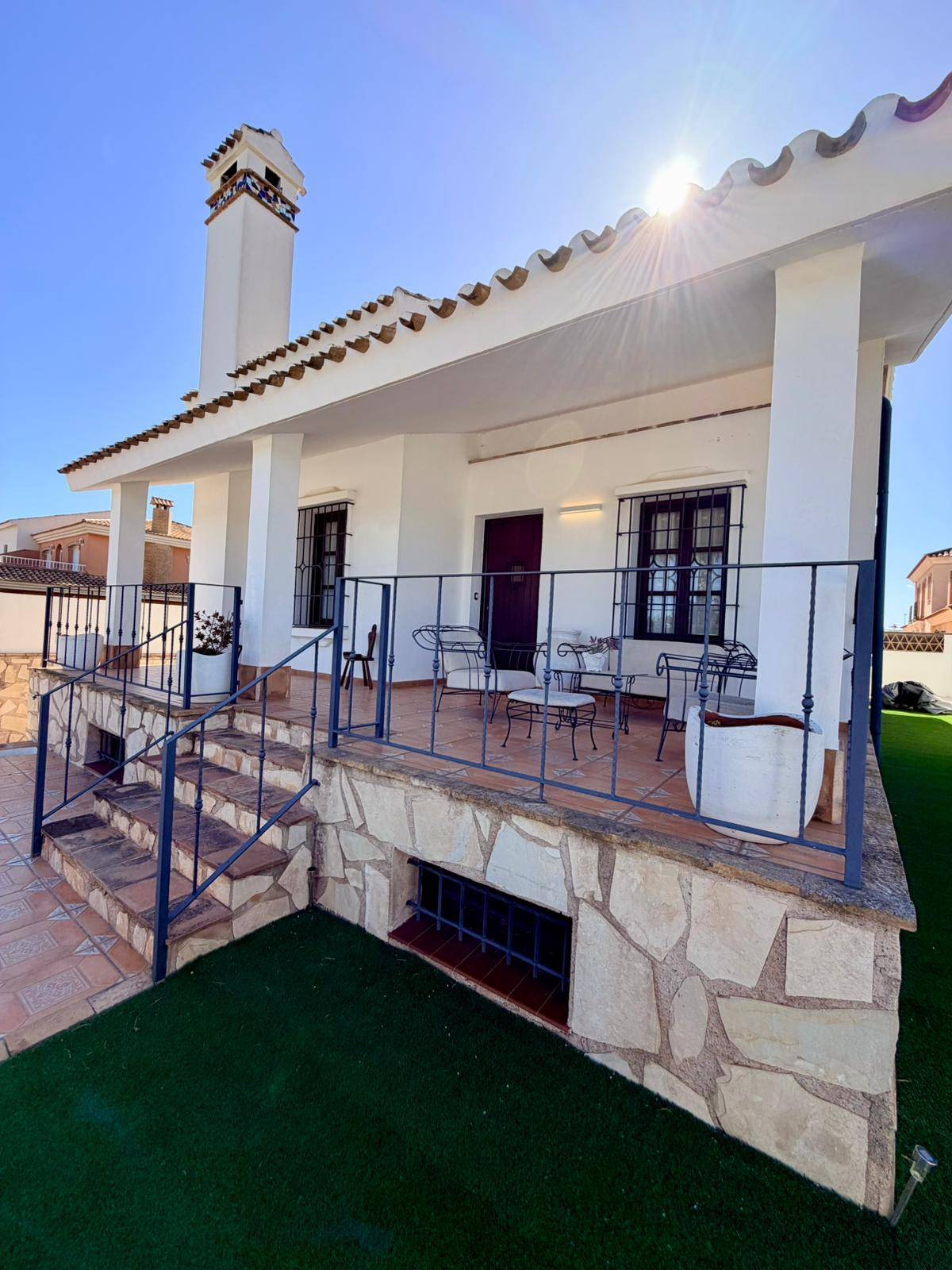 Überdachte Terrasse mit schmiedeeisernem Geländer und Zugang zum Gartenbereich.